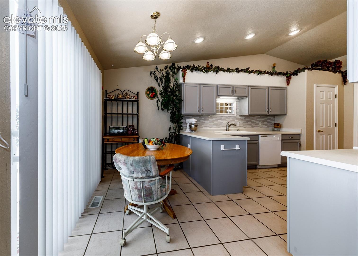 Kitchen featuring gray cabinetry, stone-look tile flooring, tiled backsplash, built-in dishwasher, and a peninsula counter