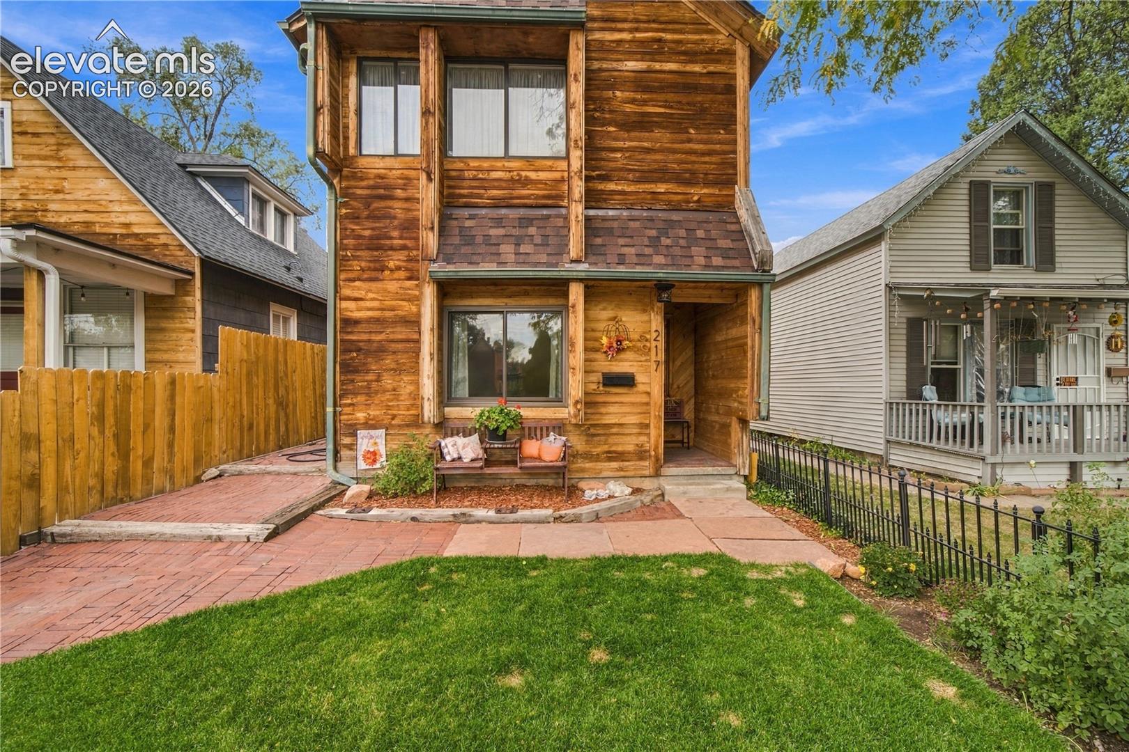 Multi-level wood-clad exterior featuring vertical timber accents, a brick-paved walkway, and a landscaped front lawn