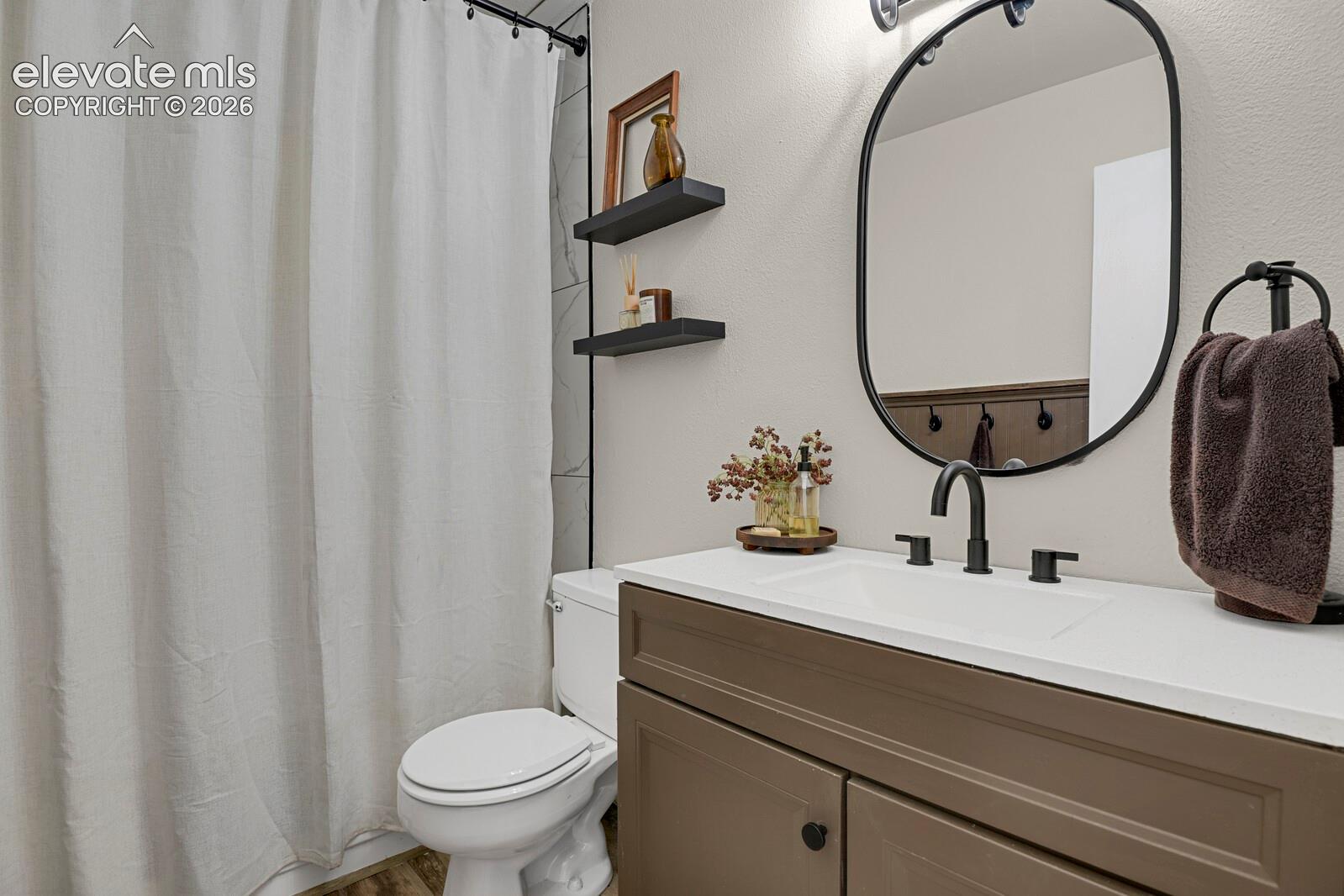 Vanity with a white countertop and integrated sink, matte black faucet, oval mirror, and dark brown cabinetry