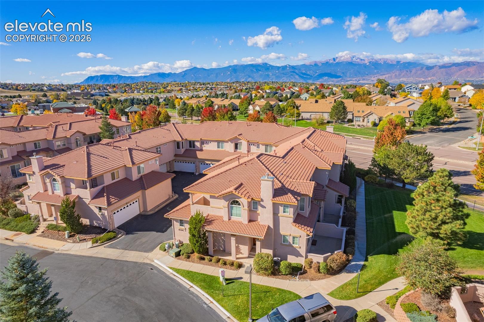 Aerial perspective of multi-unit residential structures featuring stucco exteriors, tile roofing, attached garages, and mountain backdrop