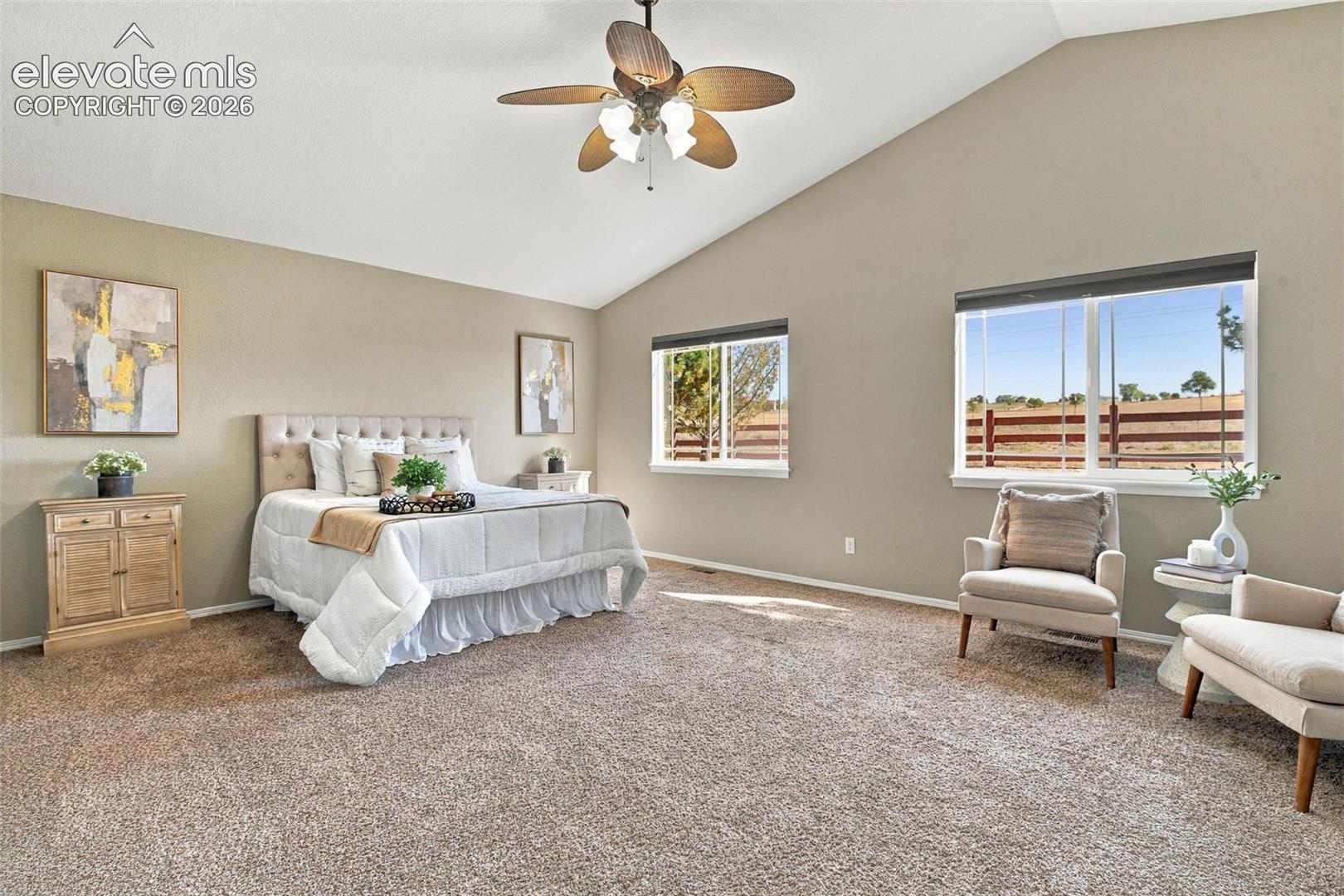 Vaulted ceiling with a ceiling fan, plush carpet flooring, and multiple windows