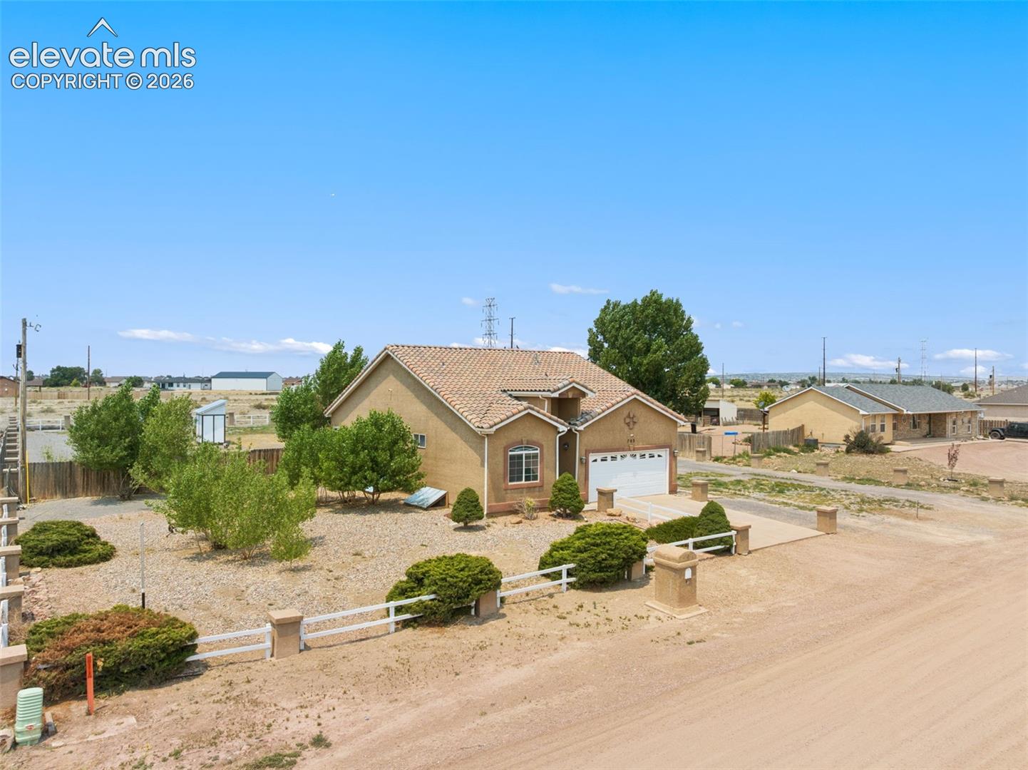 Stucco exterior featuring a clay tile roof, attached two-car garage, and white perimeter fencing