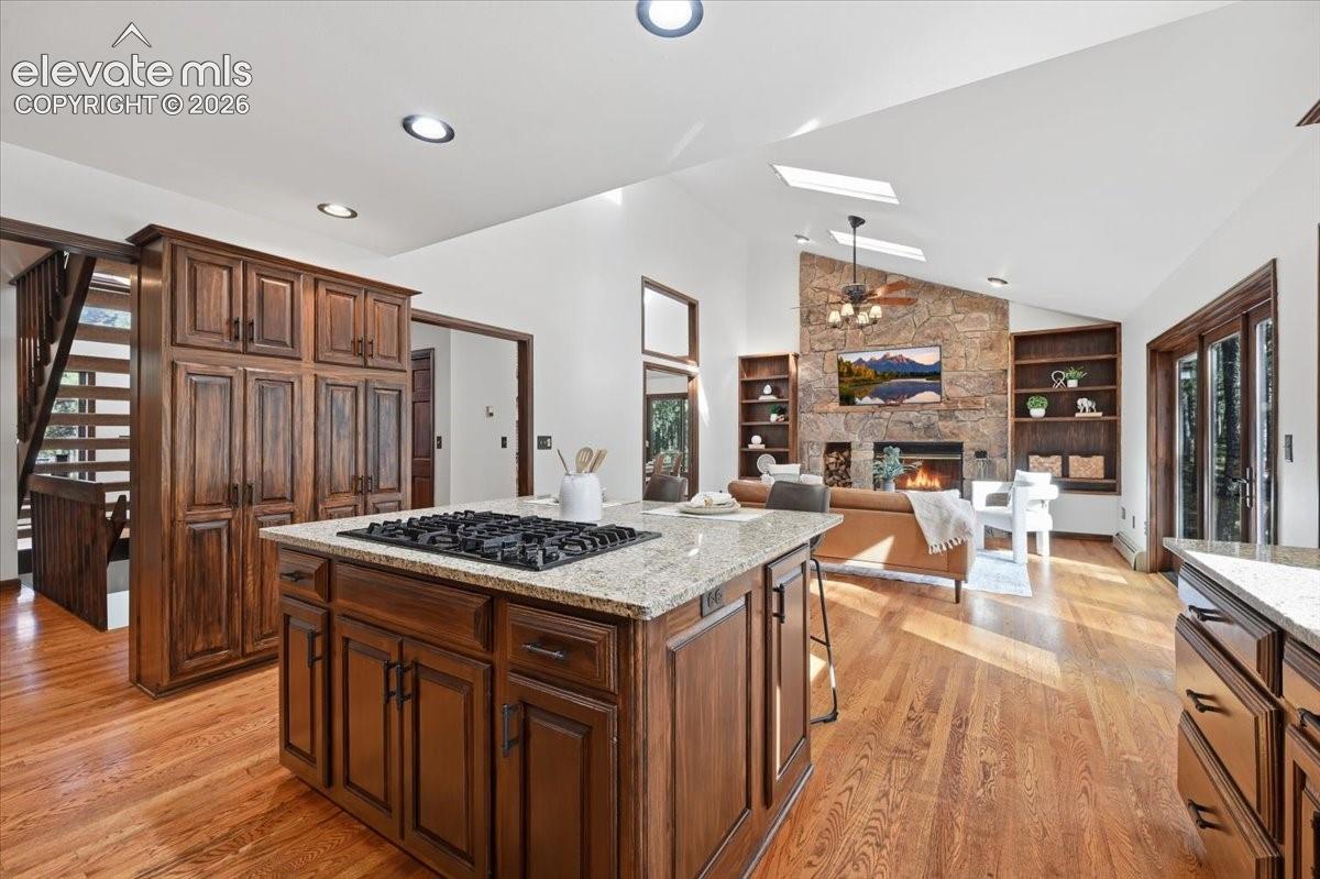 Hardwood flooring, wood cabinetry, granite countertops, and a stone-faced fireplace with built-in shelving