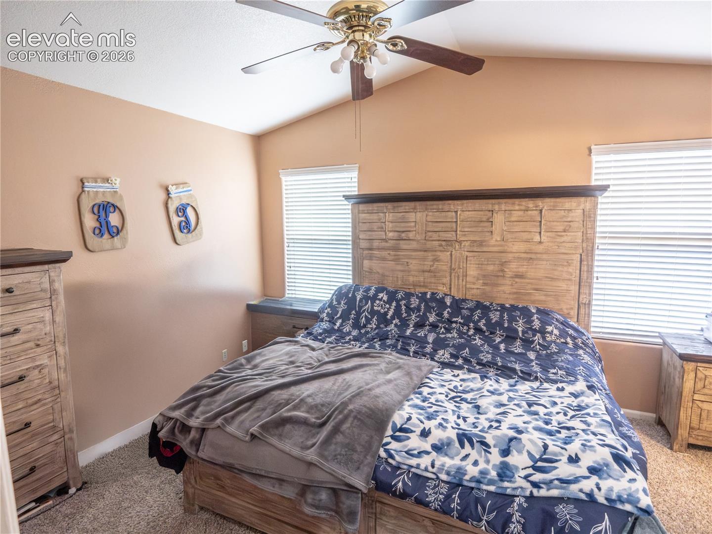 Bedroom featuring a vaulted ceiling with a ceiling fan, wall-to-wall carpeting, and two windows with blinds