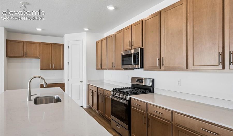 Kitchen featuring shaker-style wood cabinetry, stone countertops, stainless steel appliances, an island with an undermount sink, and recessed lighting