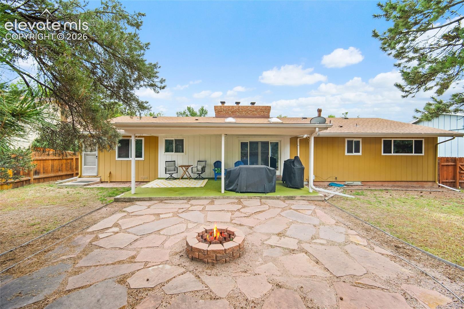 Backyard featuring a covered patio, flagstone hardscaping, a built-in masonry fire pit, and wood-panel siding