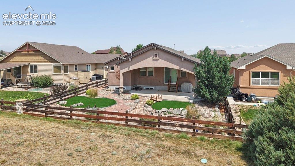 Rear exterior with a covered patio, concrete patio, and a tiered landscaped backyard featuring artificial turf and natural rock elements