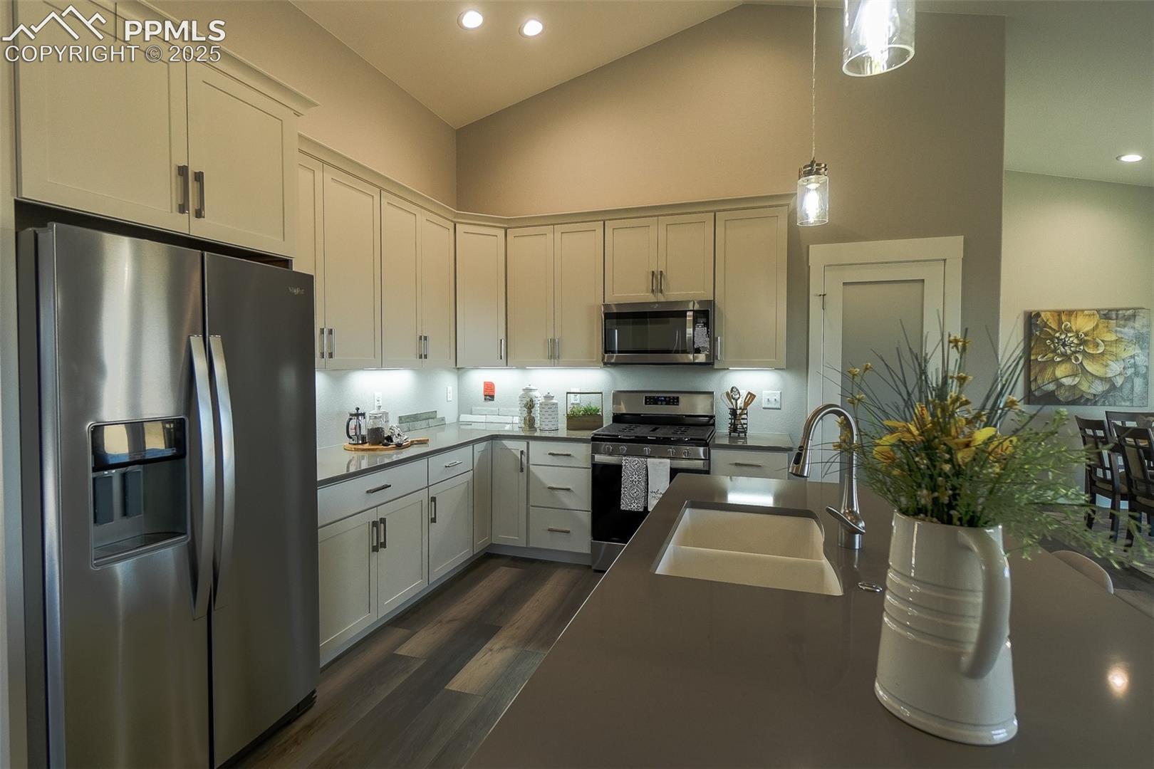 Kitchen with stainless steel appliances, LTV hardwood / wood-style flooring, pendant lighting, high vaulted ceiling, and sink