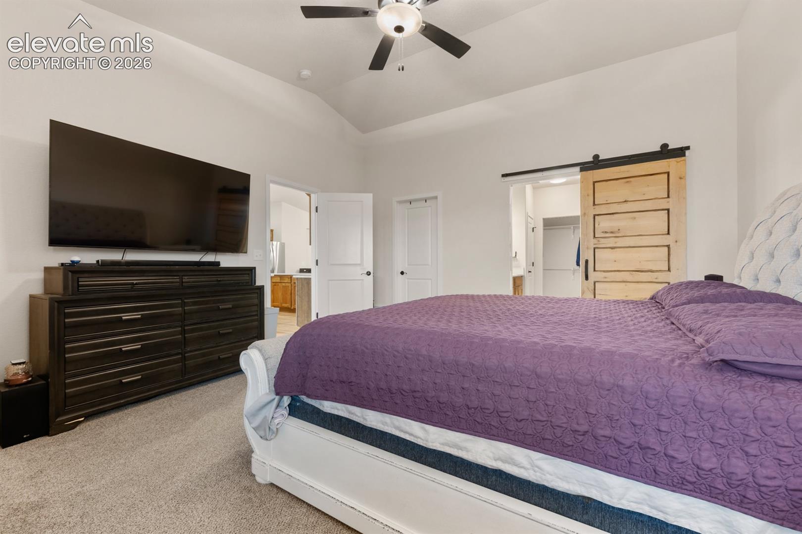 Vaulted ceilings, sliding wood barn door with matte black hardware, and ceiling fan with integrated lighting