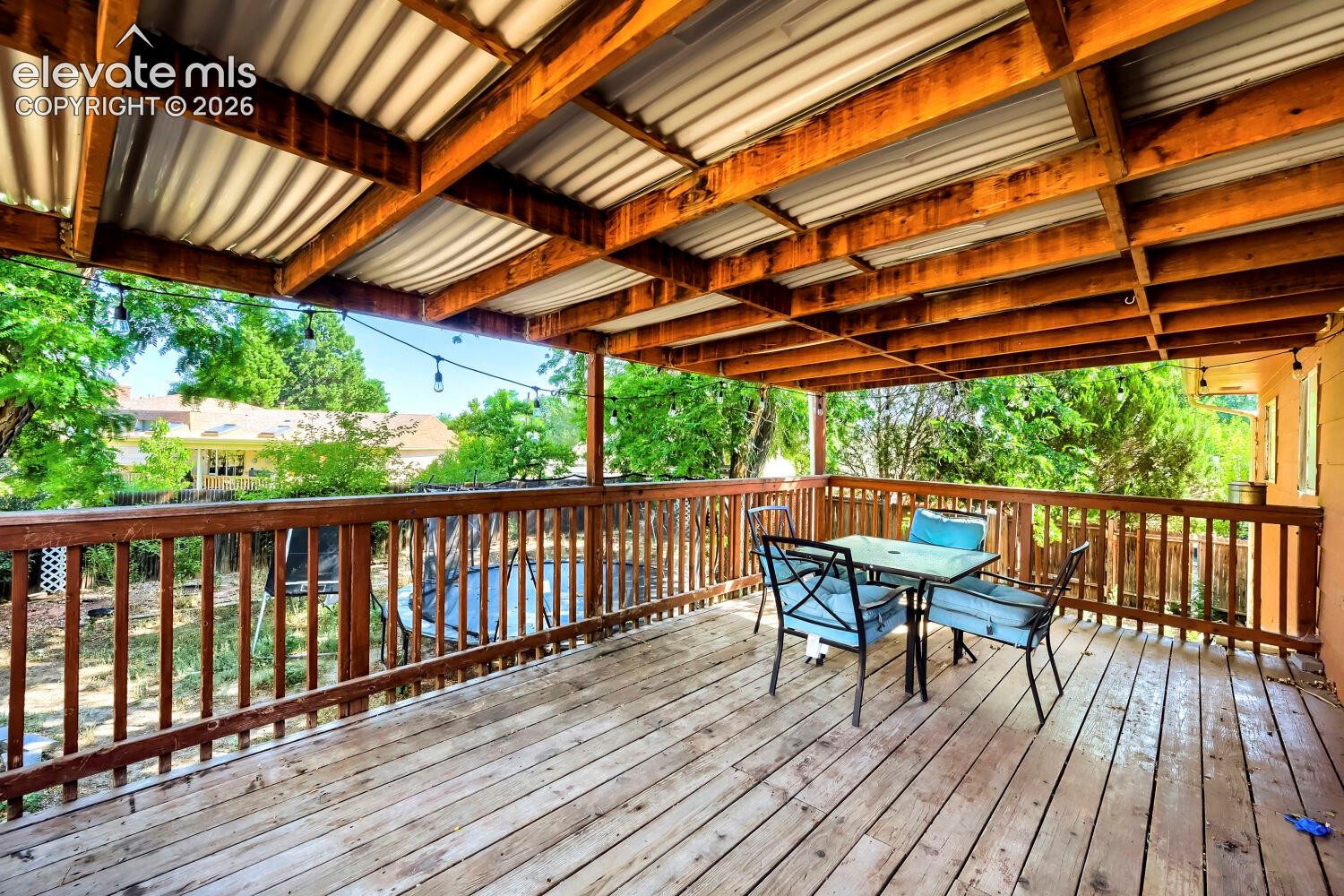 Expansive outdoor deck featuring wood-finish flooring, a robust wooden railing, and a corrugated metal roof covering