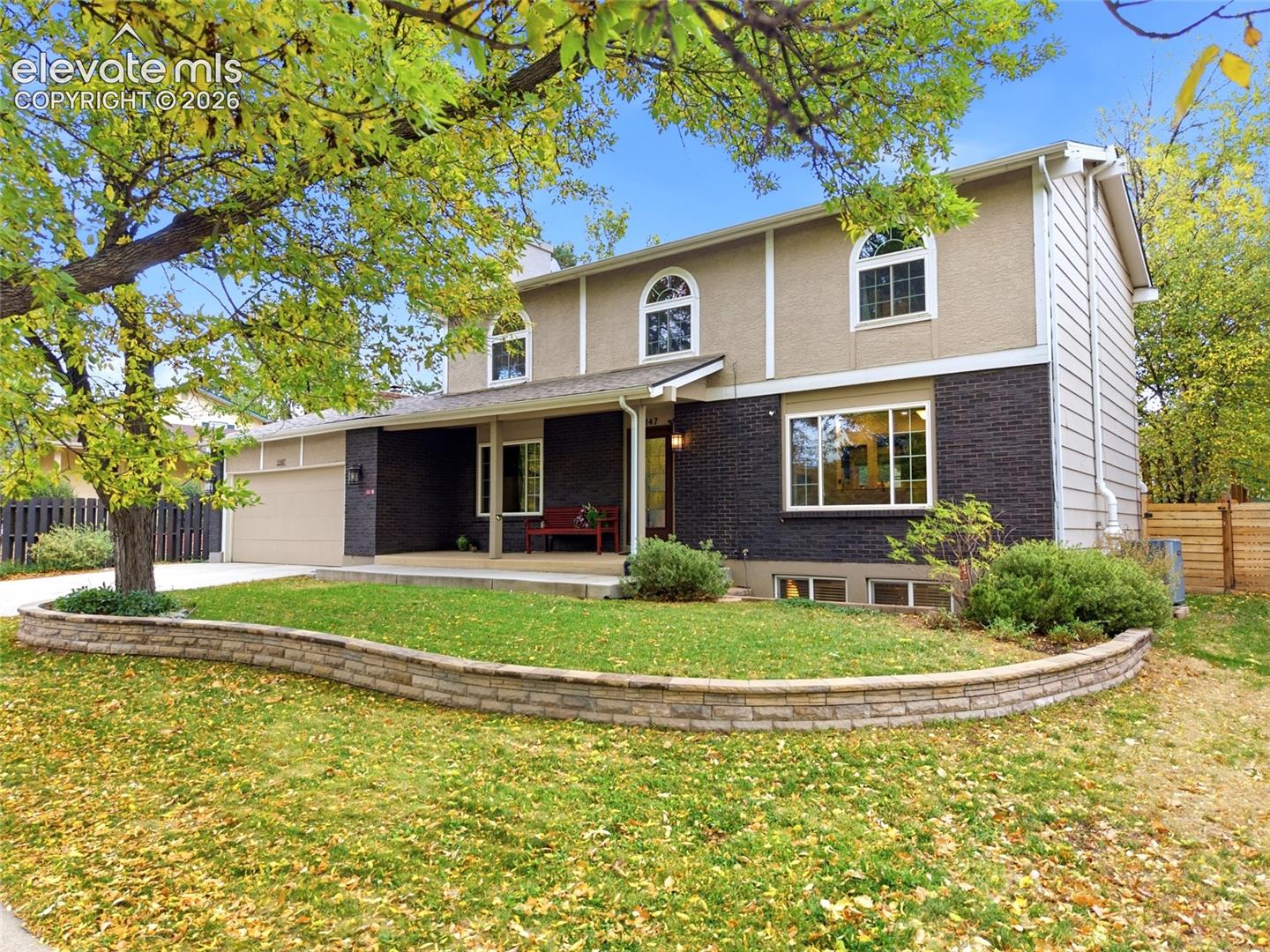 Two-story exterior featuring dark masonry siding, stone-textured retaining wall, arched window detailing, and an attached two-car garage