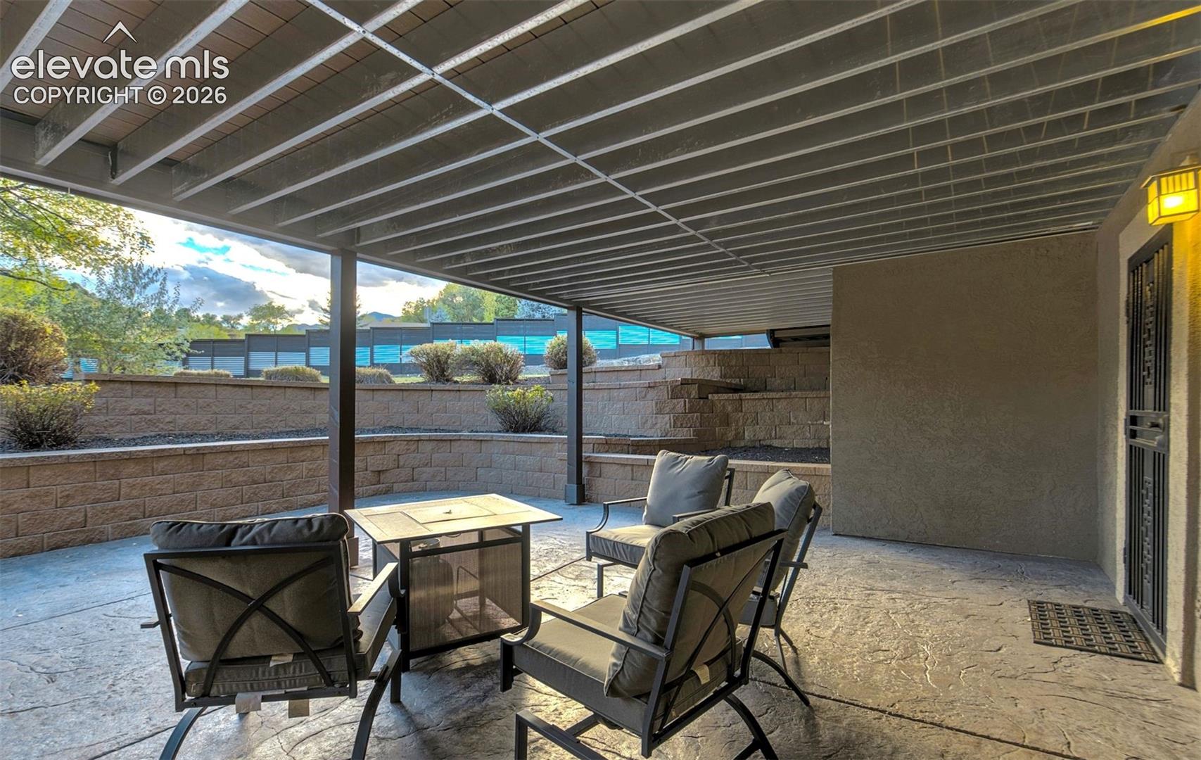 Covered patio featuring a stamped concrete floor, overhead wooden pergola, and tiered masonry retaining walls