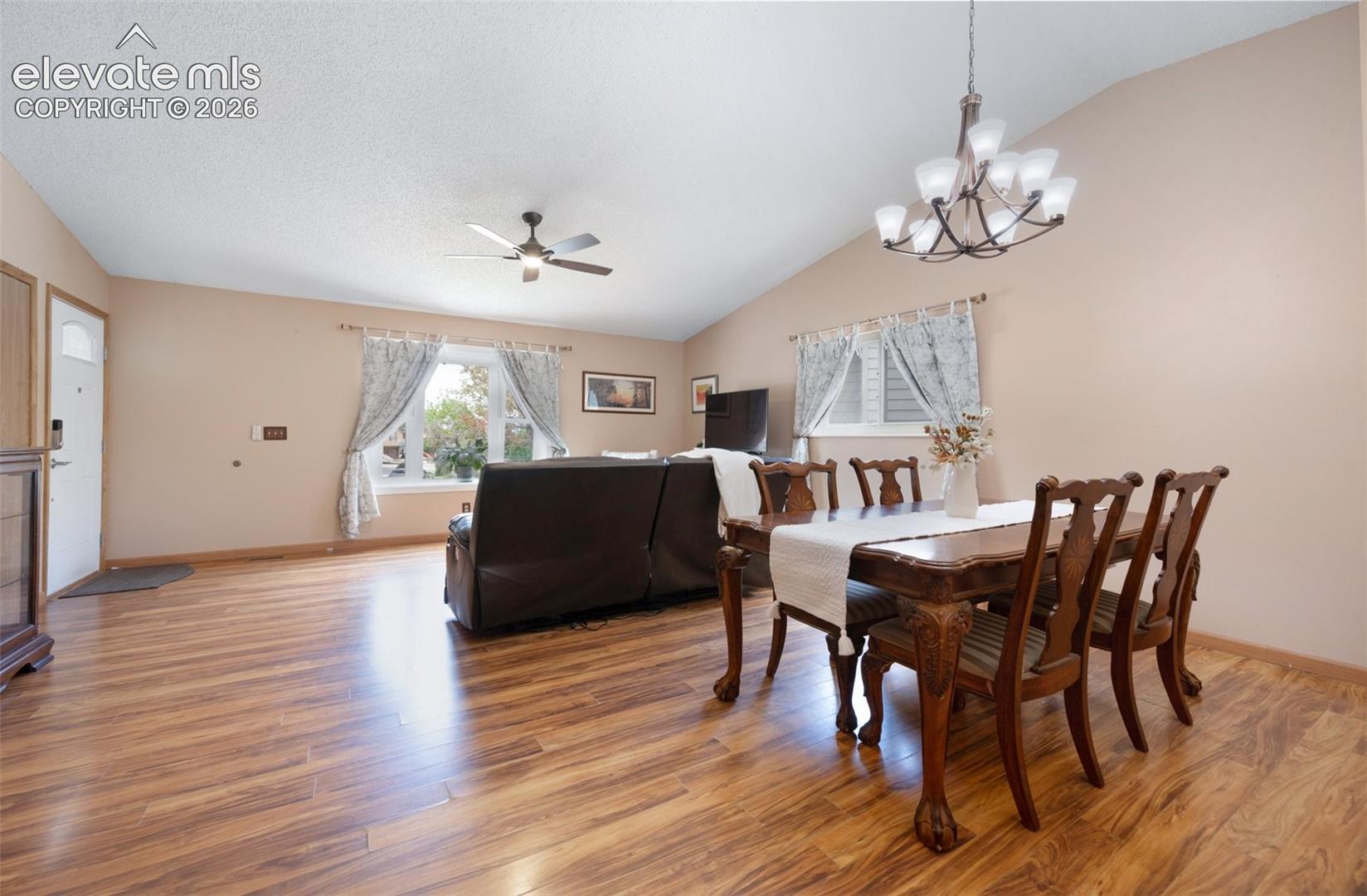 Dining room featuring lofted ceiling, light wood-style floors, a ceiling fan, a chandelier, and baseboards