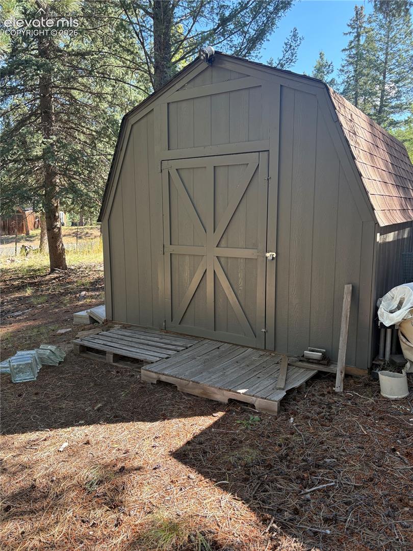 Gambrel-roof outbuilding featuring wood siding, double doors, and shingled roofing