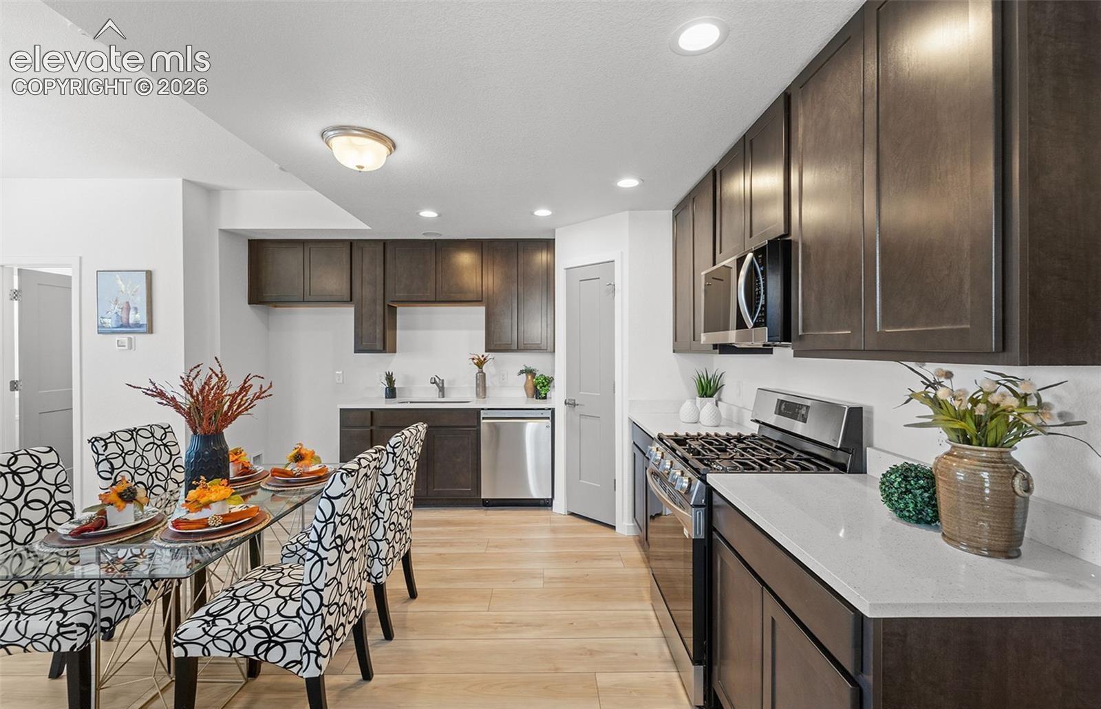 Kitchen featuring dark-finish cabinetry, light stone-composite countertops, stainless steel appliances, recessed ceiling lighting, and wood-finish flooring