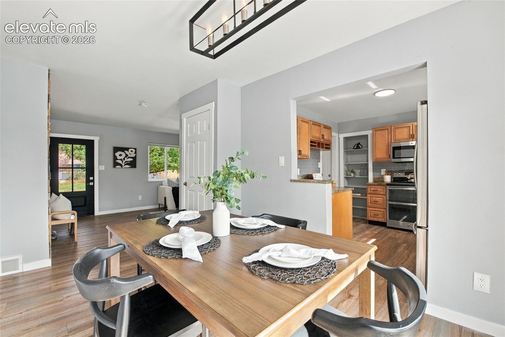 Dining area featuring wood-finish flooring, a contemporary linear chandelier, and a pass-through opening to the kitchen