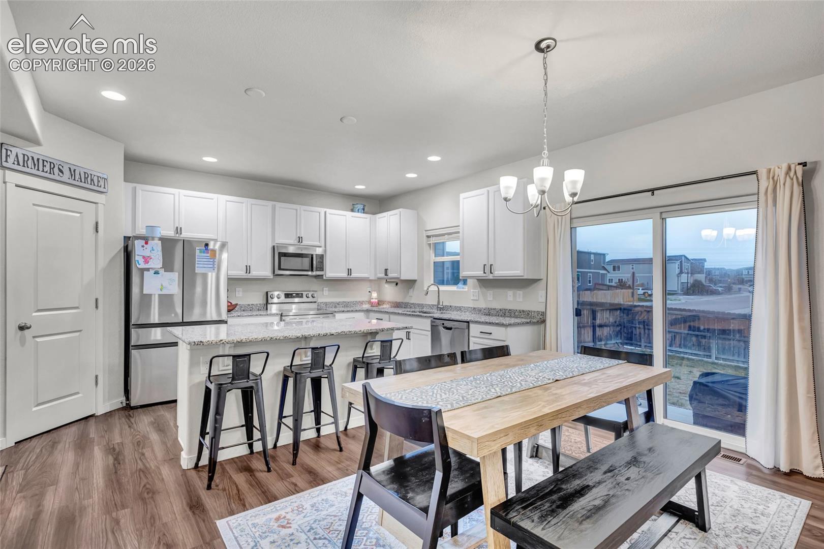 Kitchen featuring wood-finish flooring, white cabinetry, stainless steel appliances, and a central island with countertop seating