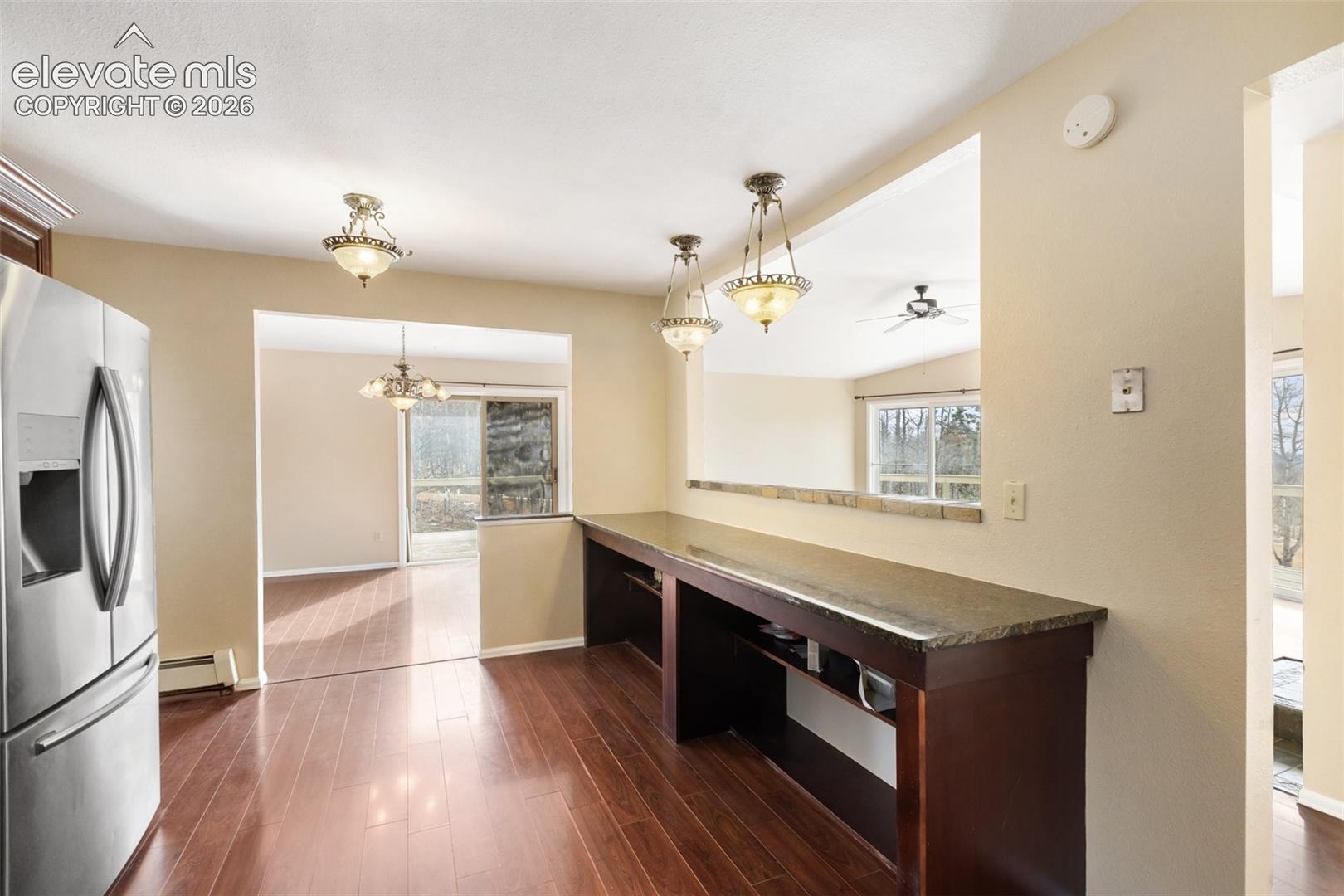 Hardwood-finish flooring, stainless steel refrigerator, built-in counter with storage, recessed pass-through opening, and decorative pendant lighting