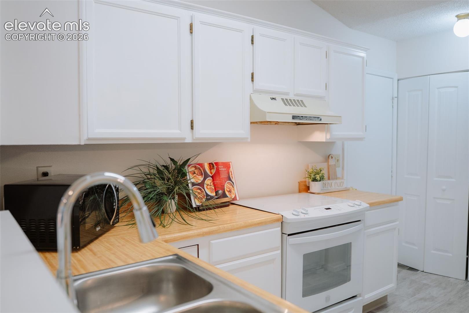 Kitchen featuring white cabinetry, light wood-finish countertops, stainless steel dual-basin sink with pull-down faucet, and white electric range with matching range hood