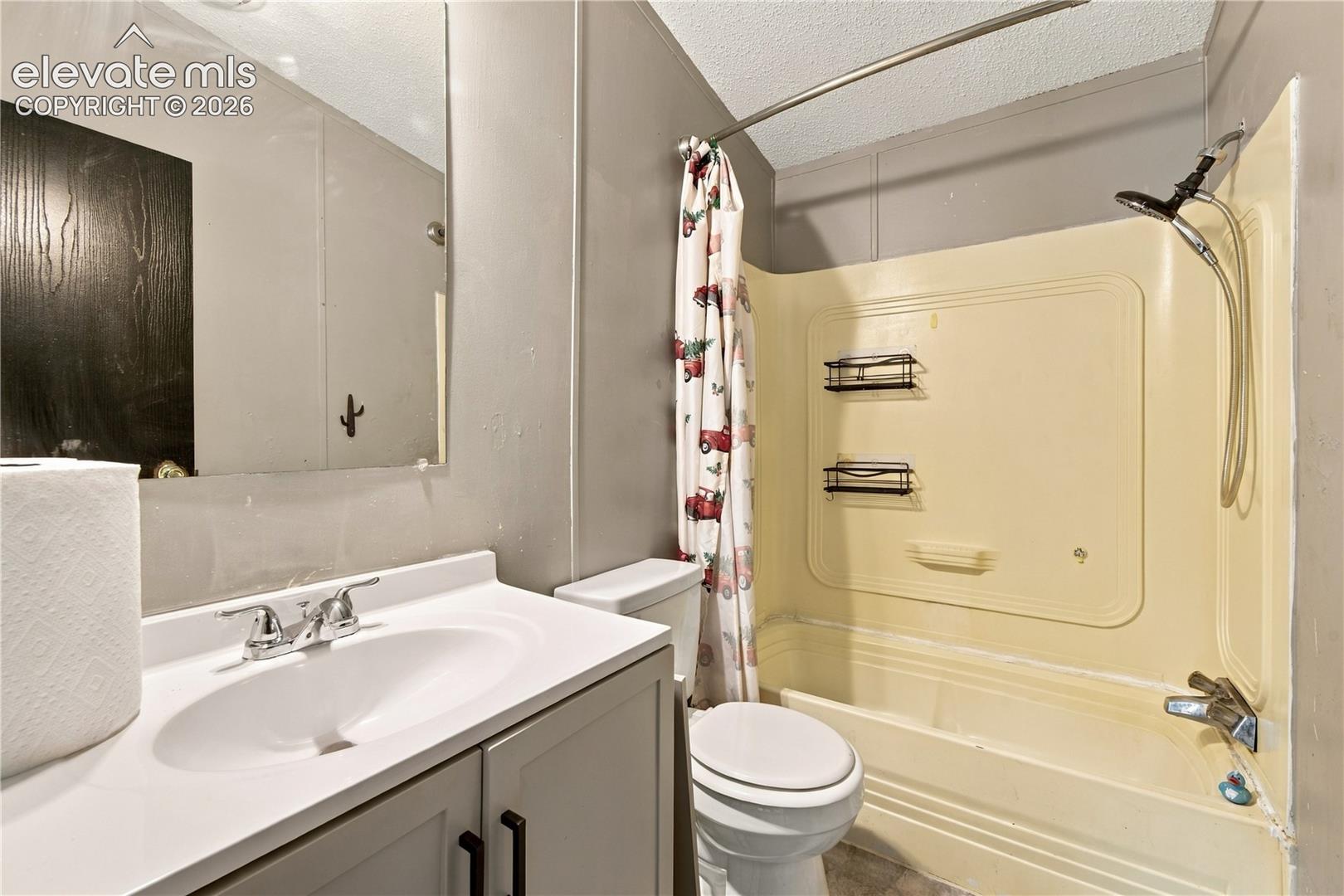 Bathroom featuring a built-in tub with an integrated shower, a vanity with a white countertop, and a wall-mounted mirror