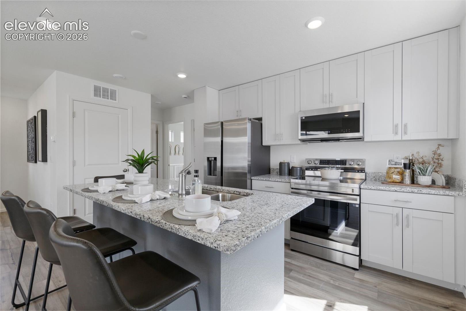 Kitchen featuring a center island, stainless steel appliances, light-toned cabinetry, granite countertops, and wood-finish flooring
*photos of a model home*