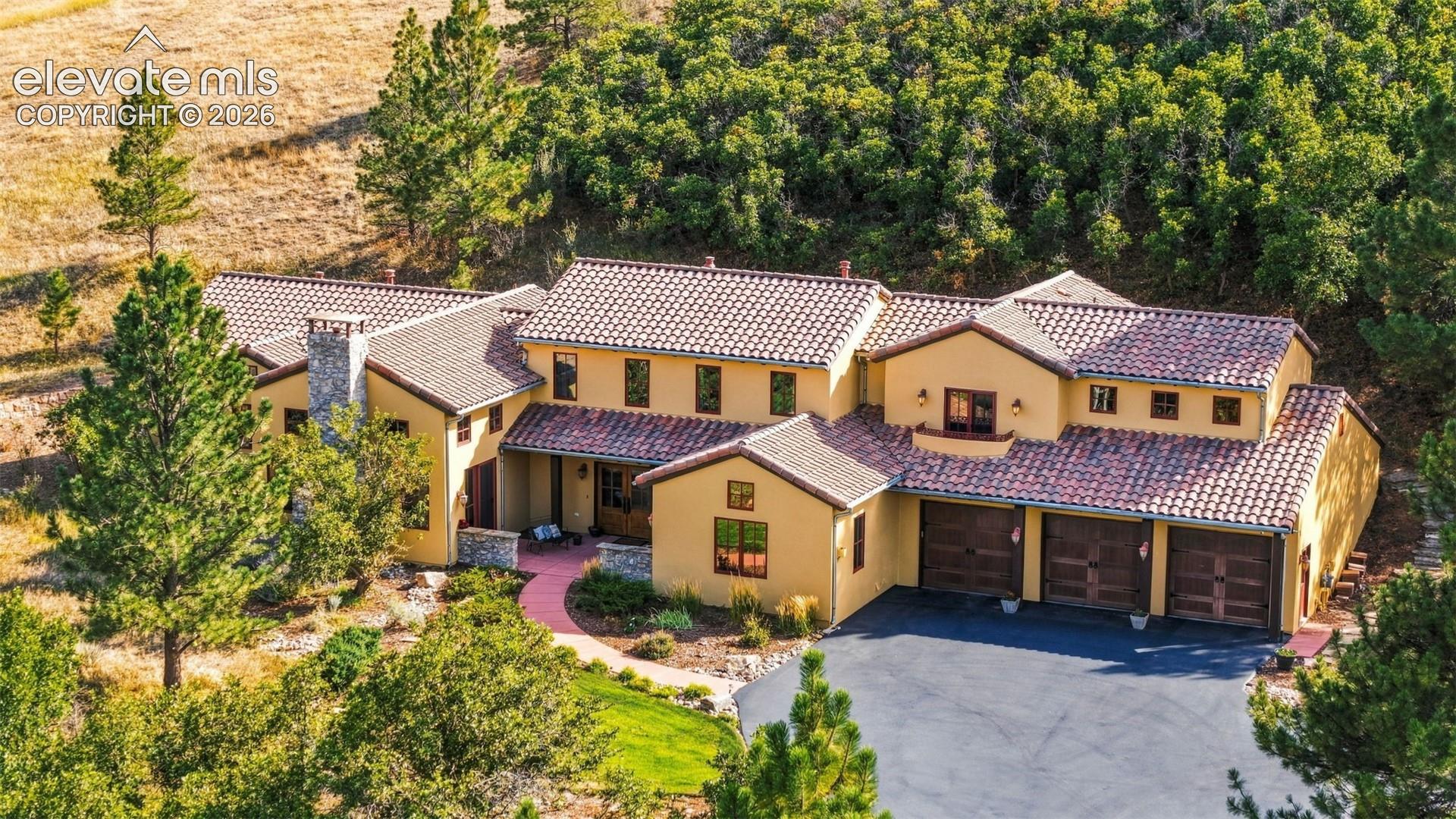 Stucco exterior with a multi-level red tile roof, three-car garage with wood-finish doors, and a stone chimney