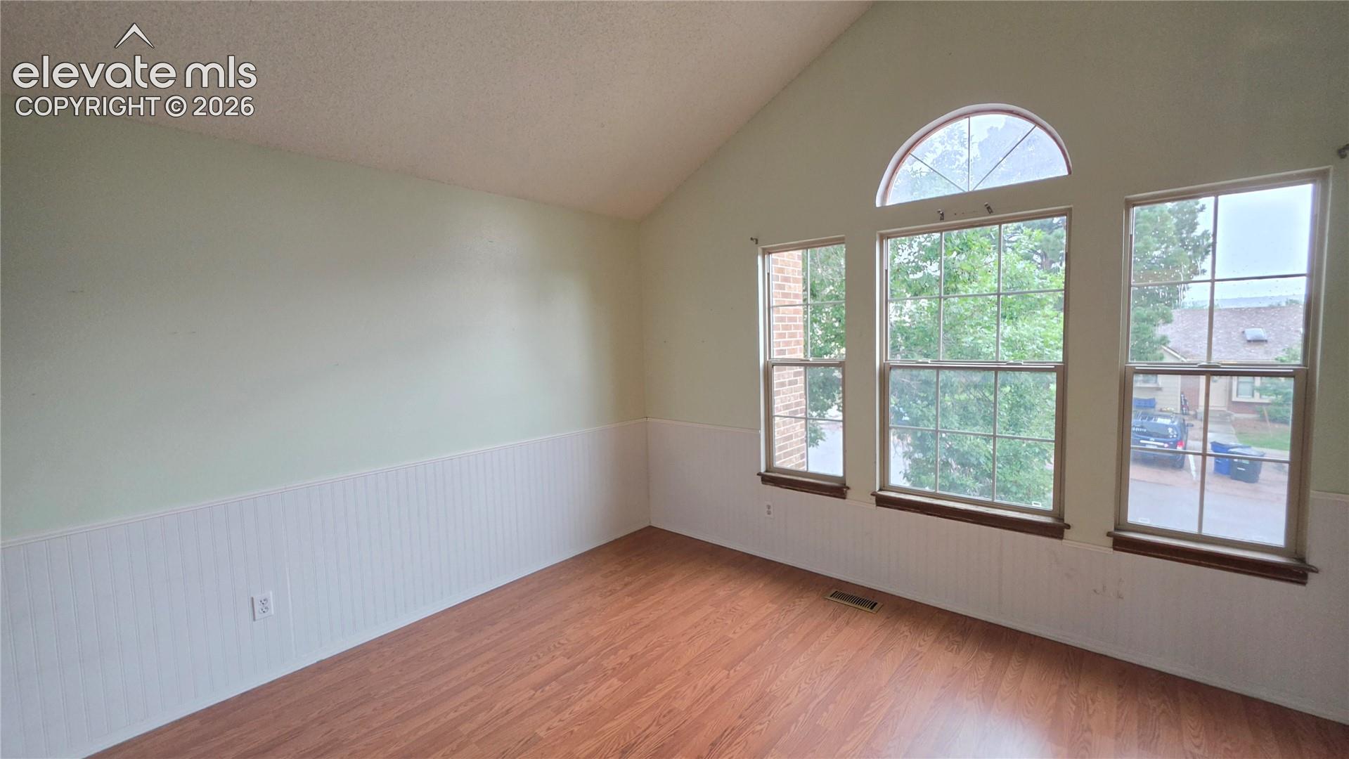 Wood-finish flooring, vaulted ceiling, three large windows, arched transom window, and wainscoting