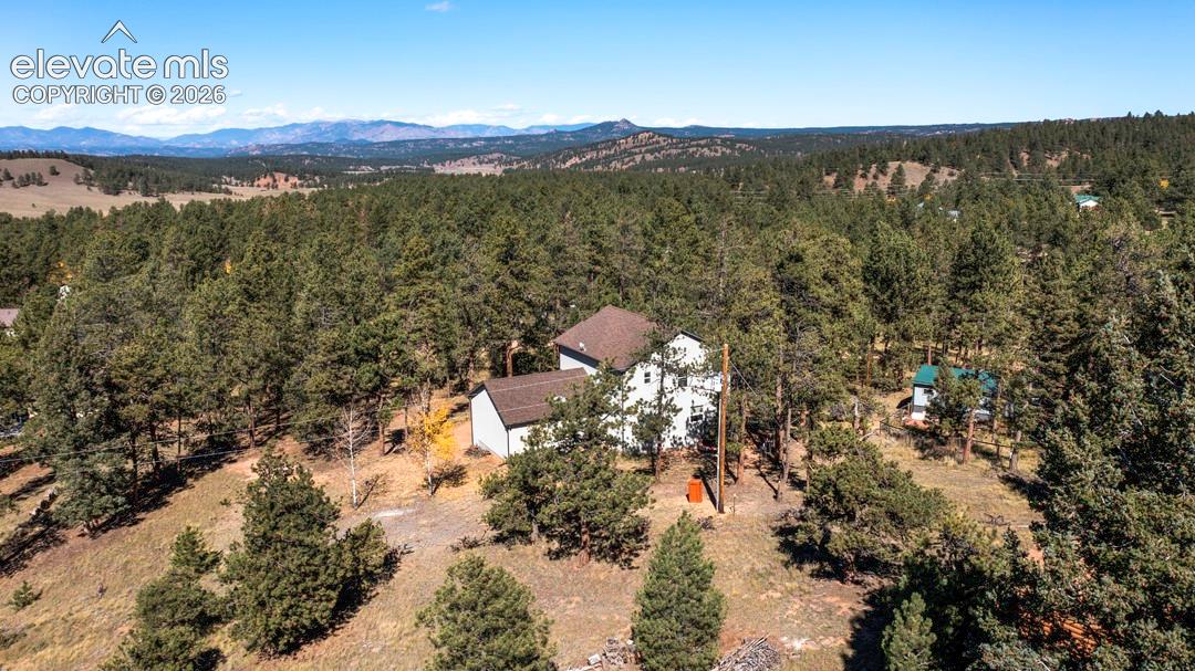 Wooded lot featuring multi-level residence with dark shingle roofing, expansive mountain backdrop, and natural terrain