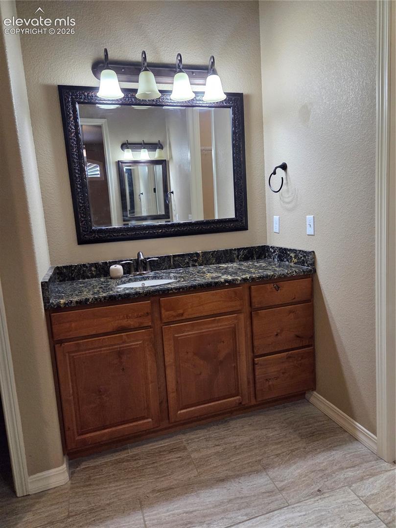 @nd master Bathroom vanity-HERS, featuring a dark stone countertop, wood-finish cabinetry, a single undermount sink, and a framed mirror with a four-light fixture