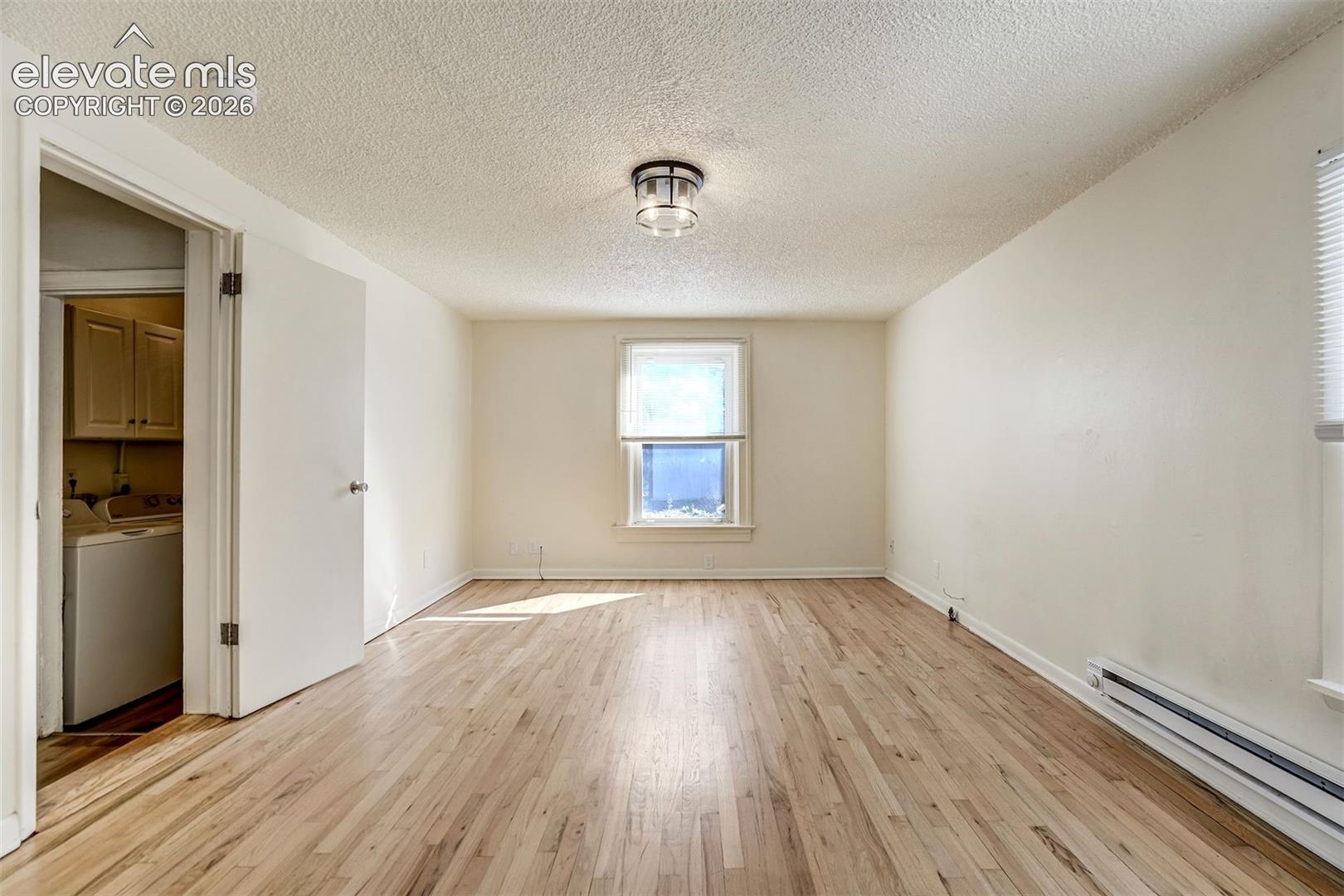 Interior room featuring wood-finish flooring, a central drum-style light fixture, a single-hung window, and a door opening to a utility space with built-in cabinetry