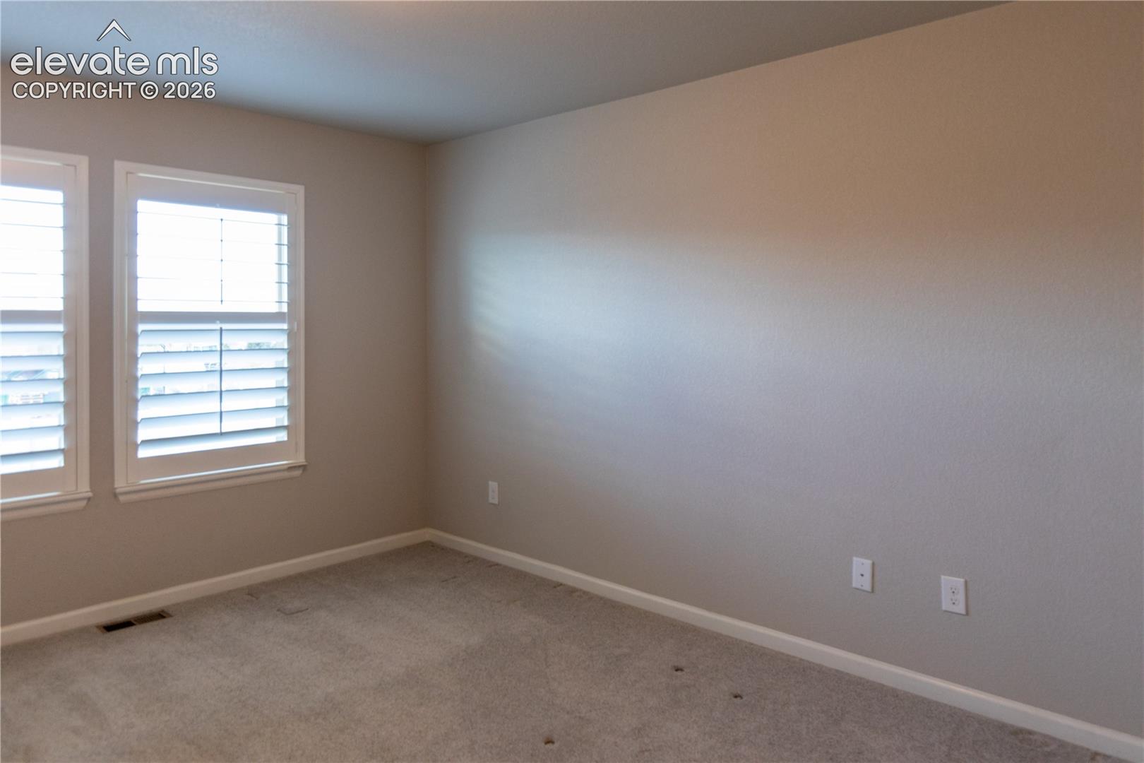 Room featuring neutral-toned walls, carpeting, and two windows outfitted with plantation shutters