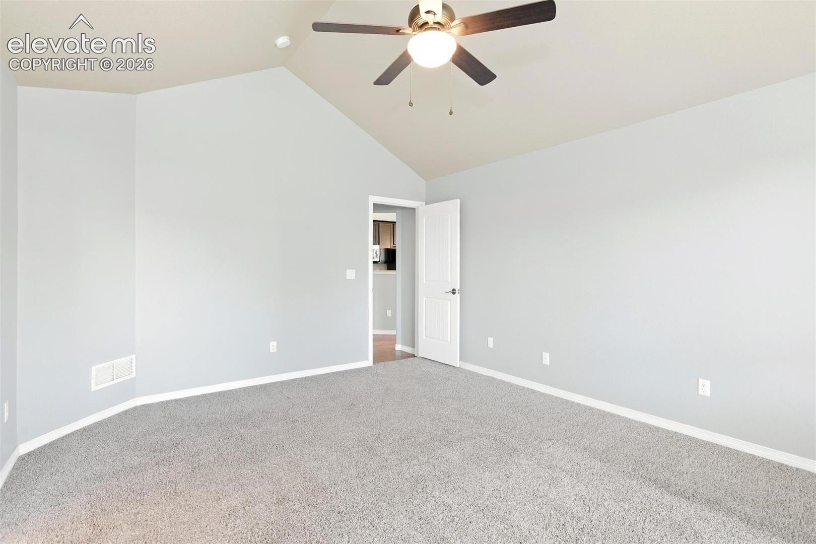 Vaulted ceiling featuring a central lighted ceiling fan, neutral wall tones, and neutral-toned carpeting