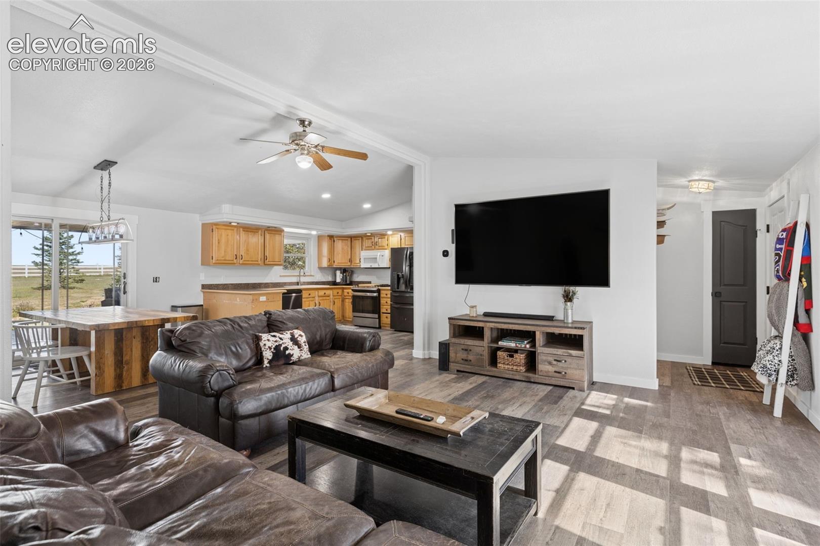 Open-concept living space featuring vaulted ceilings, wood-finish flooring, and natural lighting through glass sliding doors