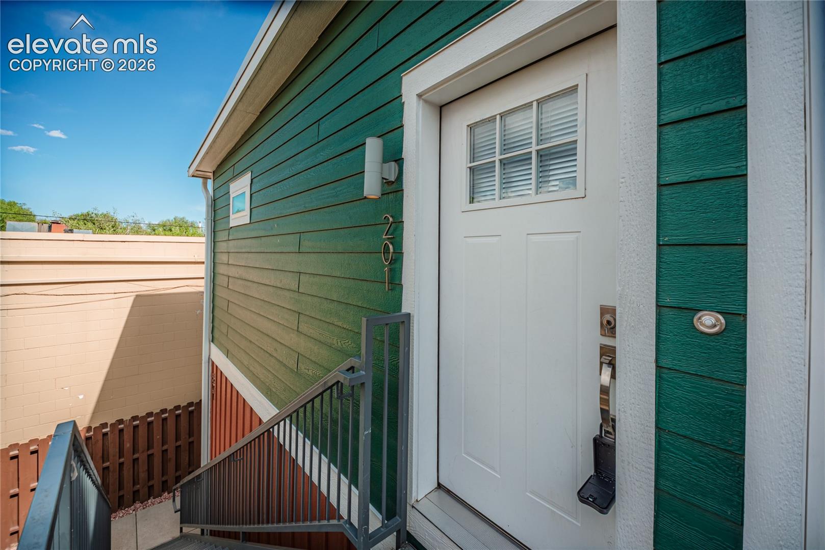 Entryway featuring a paneled door with glass inserts, wall-mounted exterior lighting, and contrasting green and red horizontal siding