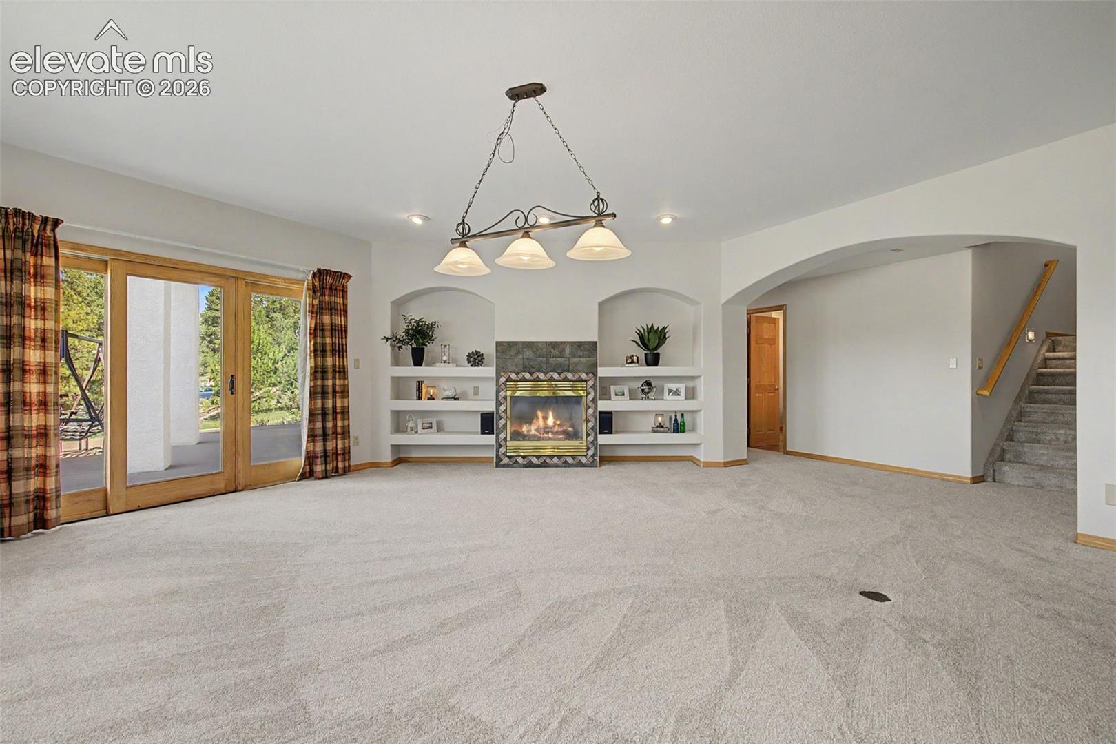 Spacious room featuring light-colored carpeting and a stone-faced fireplace with a decorative mantel