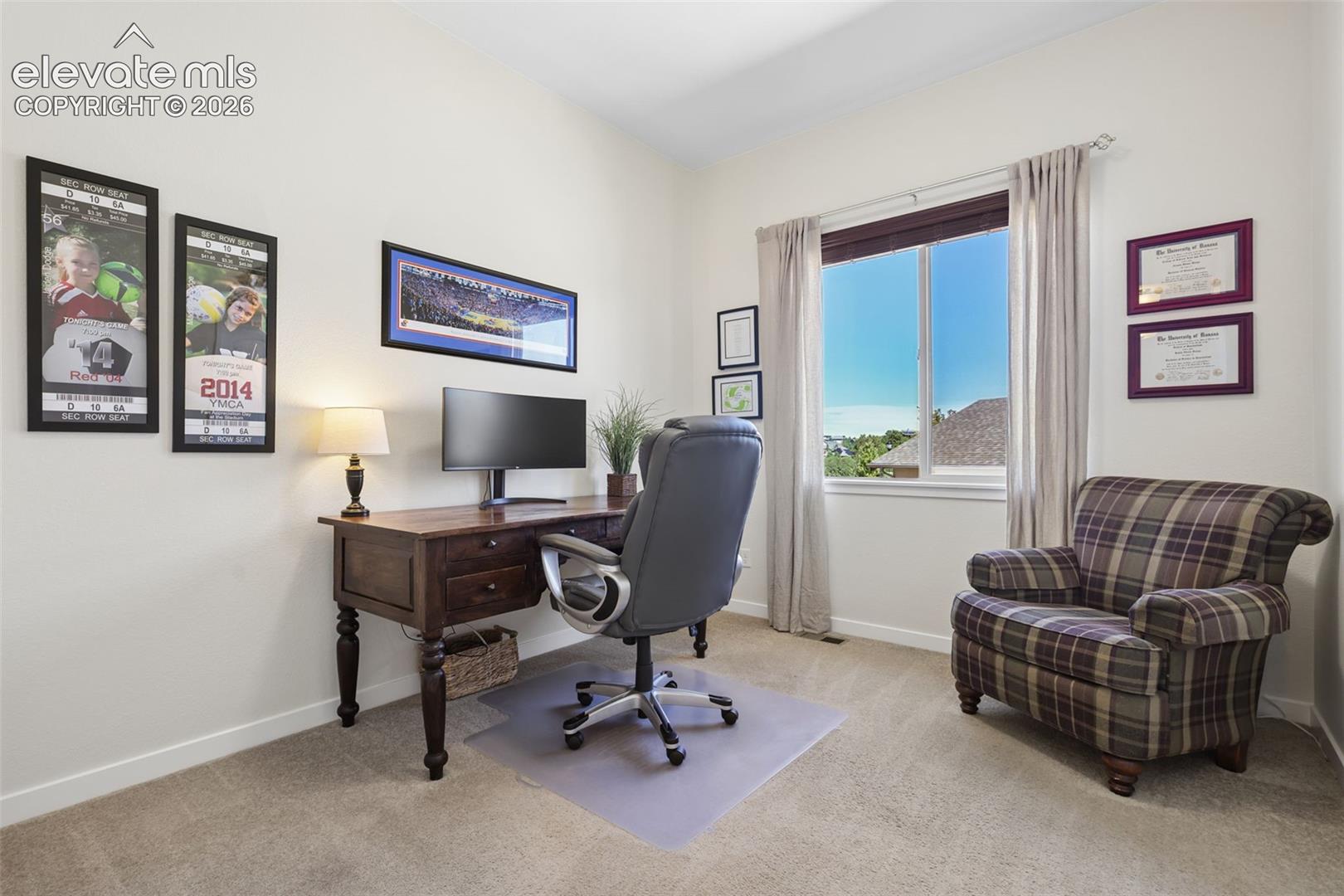 Bright home office featuring a wood-finish desk with turned legs, upholstered office chair, and plush seating area with plaid upholstery