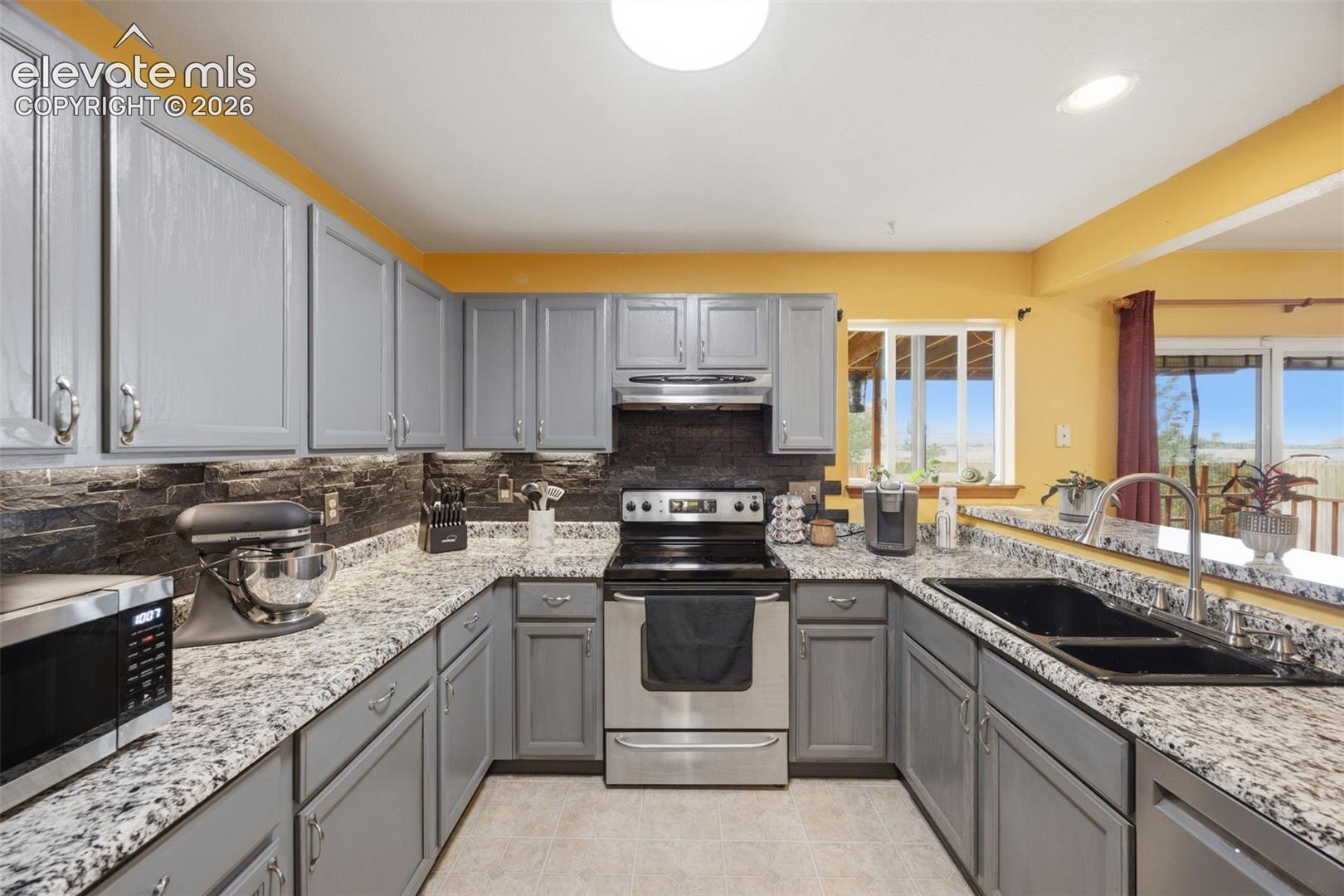 U-shaped kitchen featuring grey cabinetry, granite-finish countertops, black subway tile backsplash, and stainless steel appliances