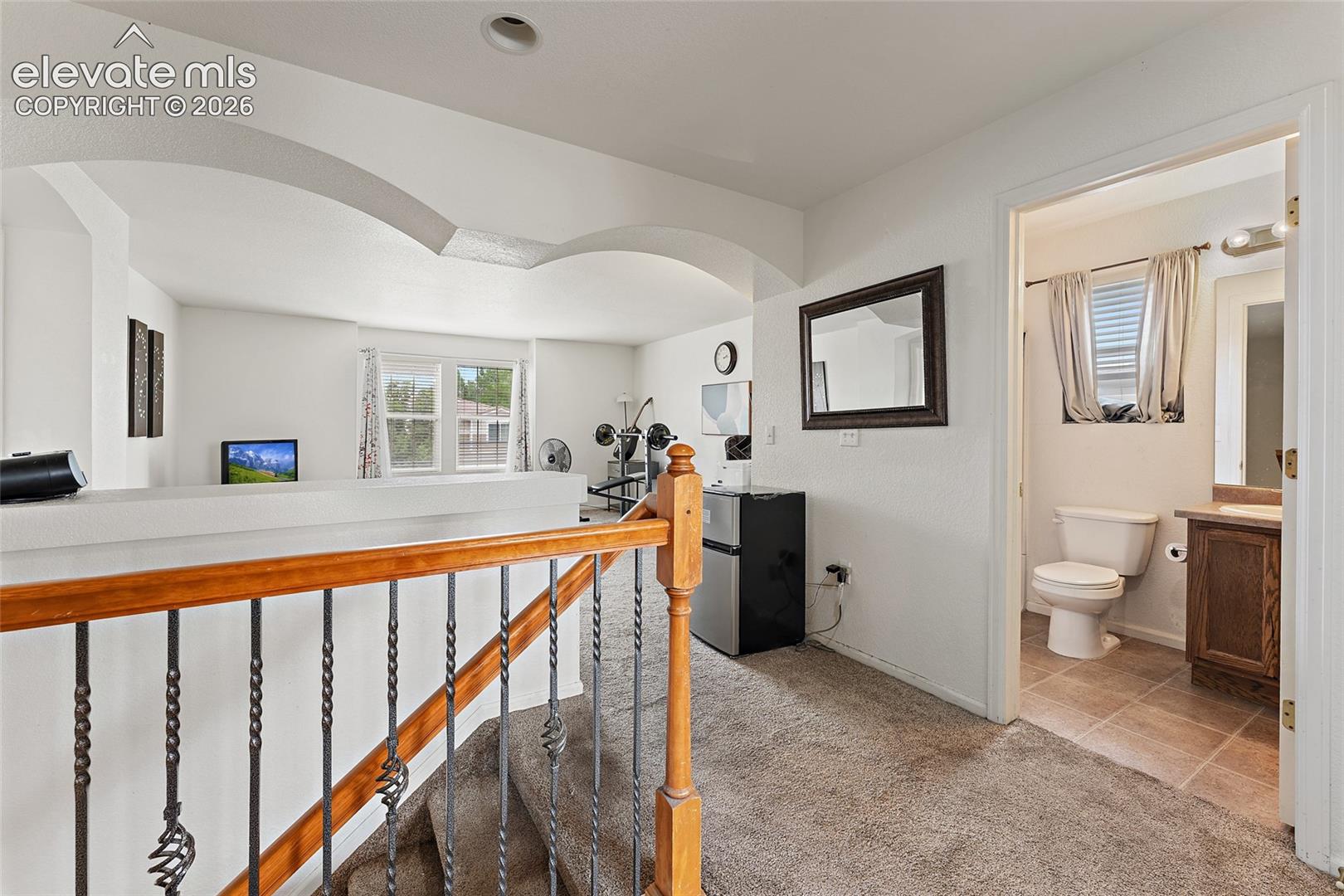 Staircase featuring a wooden handrail with decorative metal balusters and a wide archway with architectural detailing