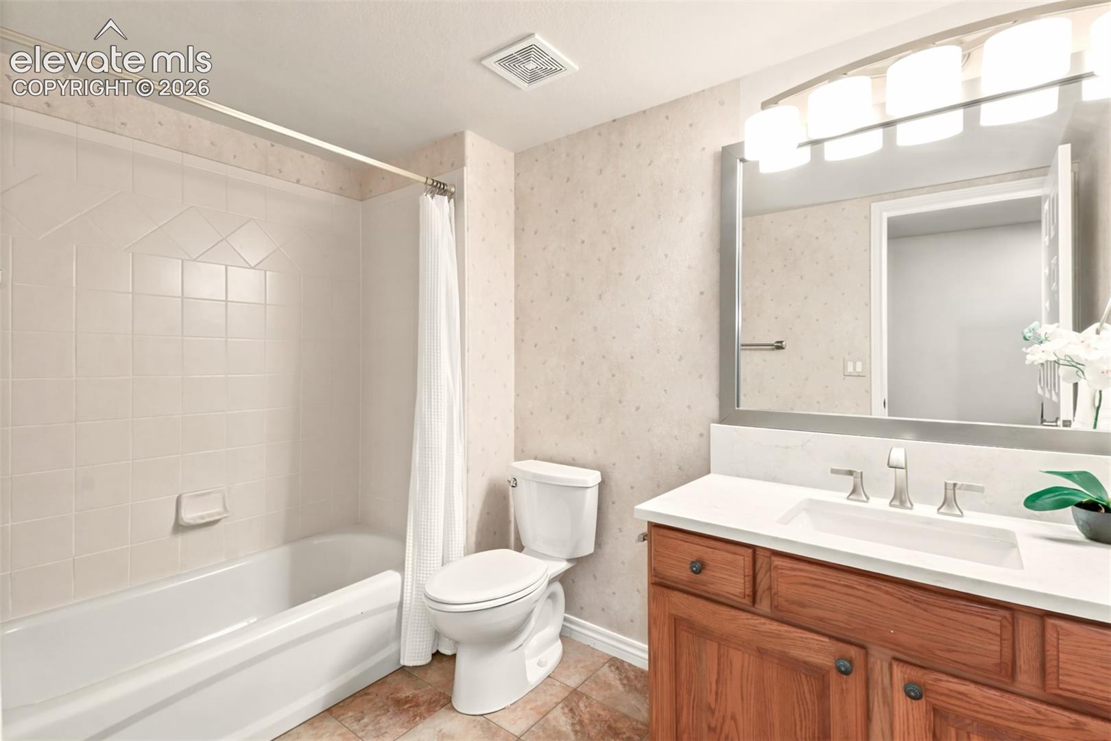 Bathroom featuring a wooden vanity with a stone countertop, integrated rectangular sink, large wall-mounted mirror, multi-light fixture, and a tile-surround bathtub