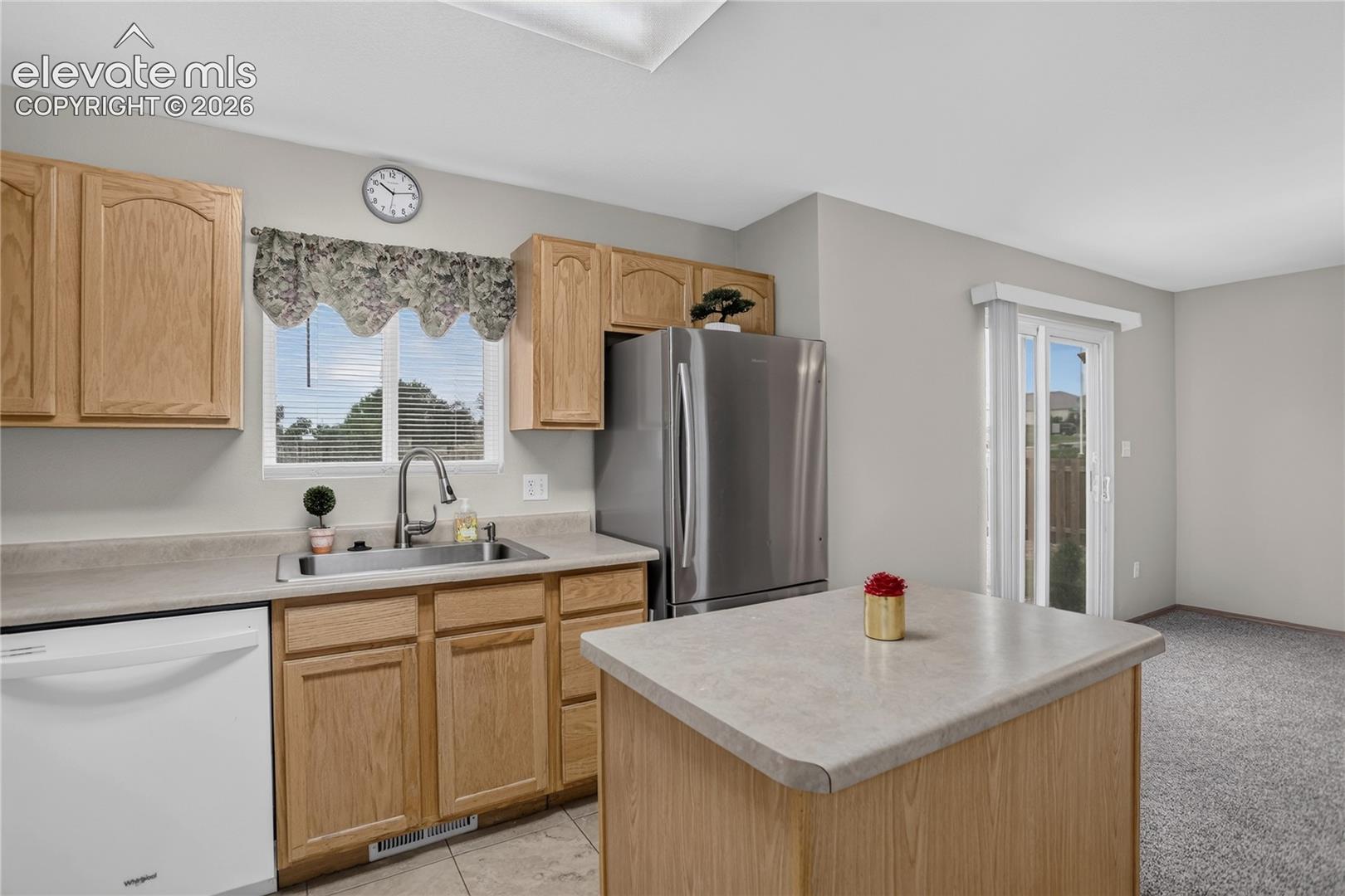 Kitchen featuring natural wood-finish cabinetry, stainless steel refrigerator, white dishwasher, and a center island with a light-toned countertop