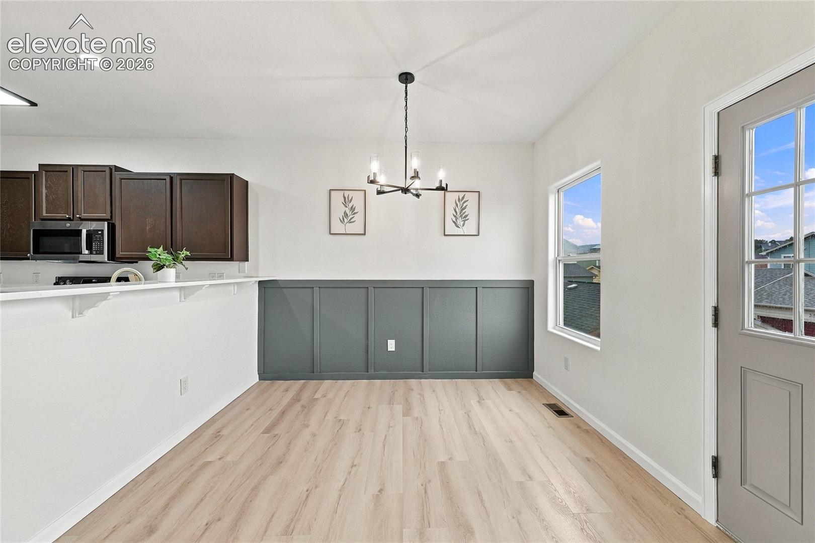 Dining area featuring wood-finish flooring, dark-toned wainscoting, an iron-finish chandelier, and a multi-pane exterior door