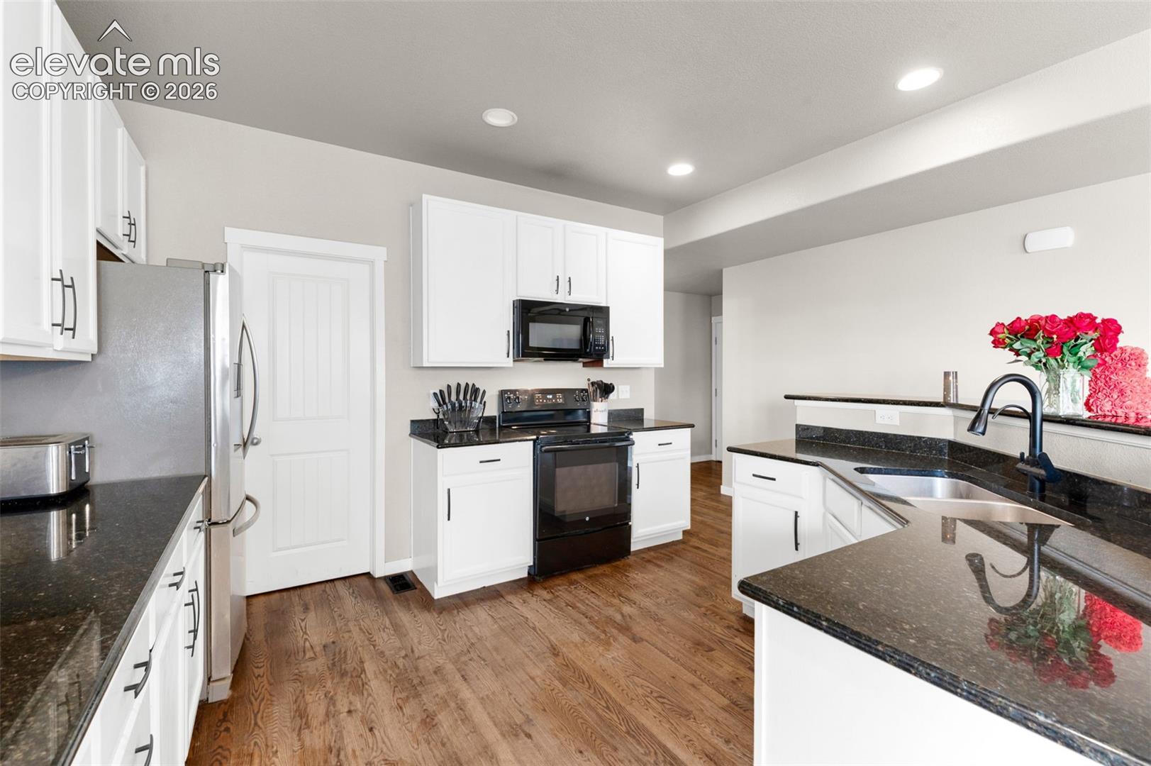 Kitchen featuring white shaker-style cabinetry, dark stone countertops, wood-finish flooring, recessed lighting, and a dual-basin stainless steel sink with a matte black faucet