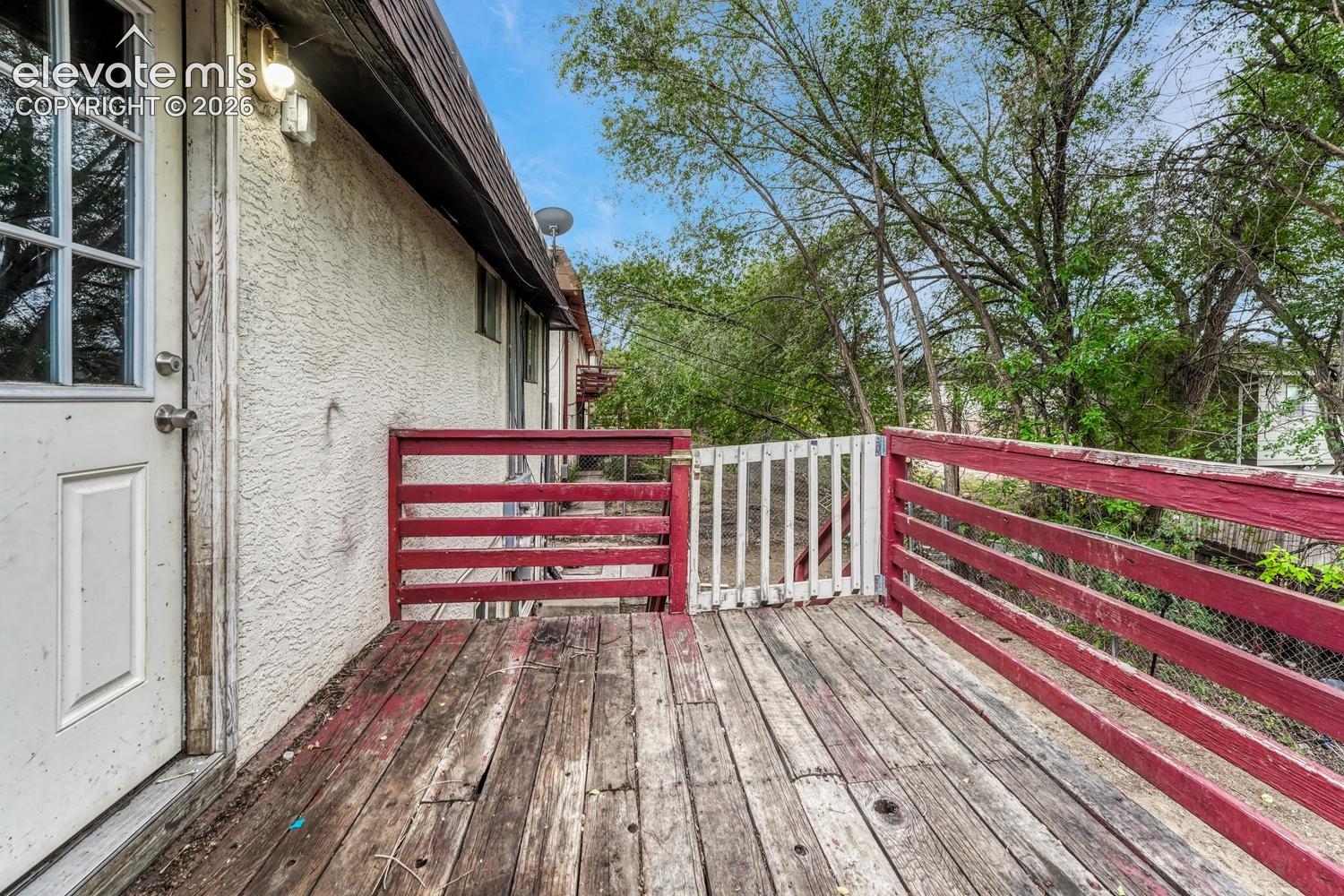 Wood-finish deck with red and white railing, featuring a privacy gate and exterior wall lighting