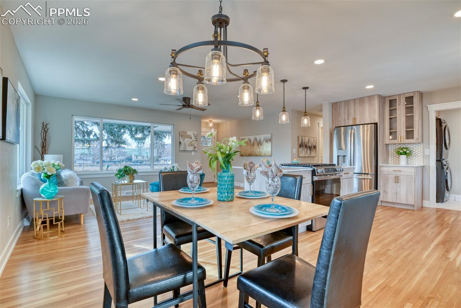 Dining area with a chandelier, light wood finished floors, stacked washer and dryer, and ceiling fan
