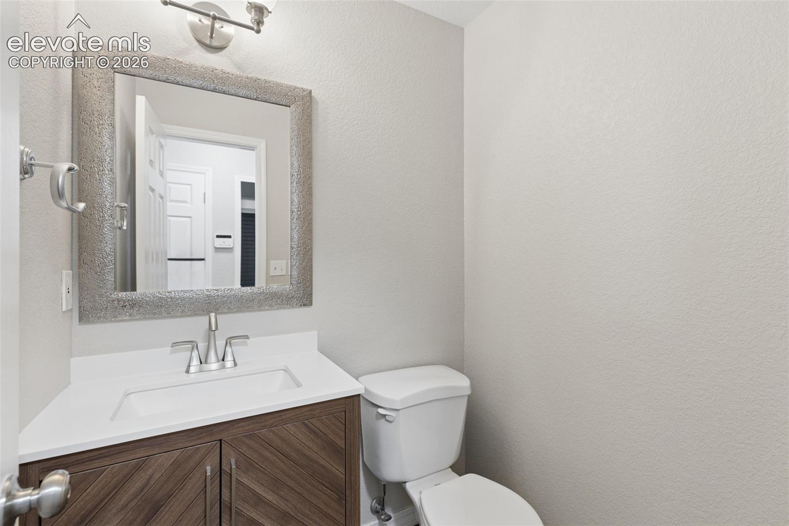 Vanity featuring wood-finish cabinetry with diagonal detailing, a solid-surface countertop, an integrated rectangular basin, a textured metallic-frame mirror, and brushed-finish hardware