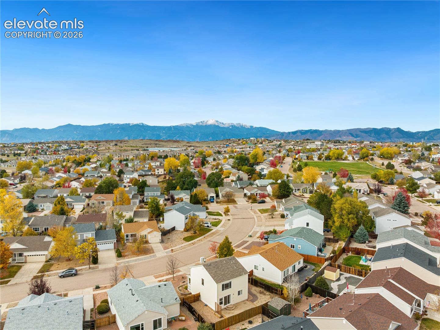 Aerial perspective of a residential neighborhood featuring prominent mountain backdrops and mature trees