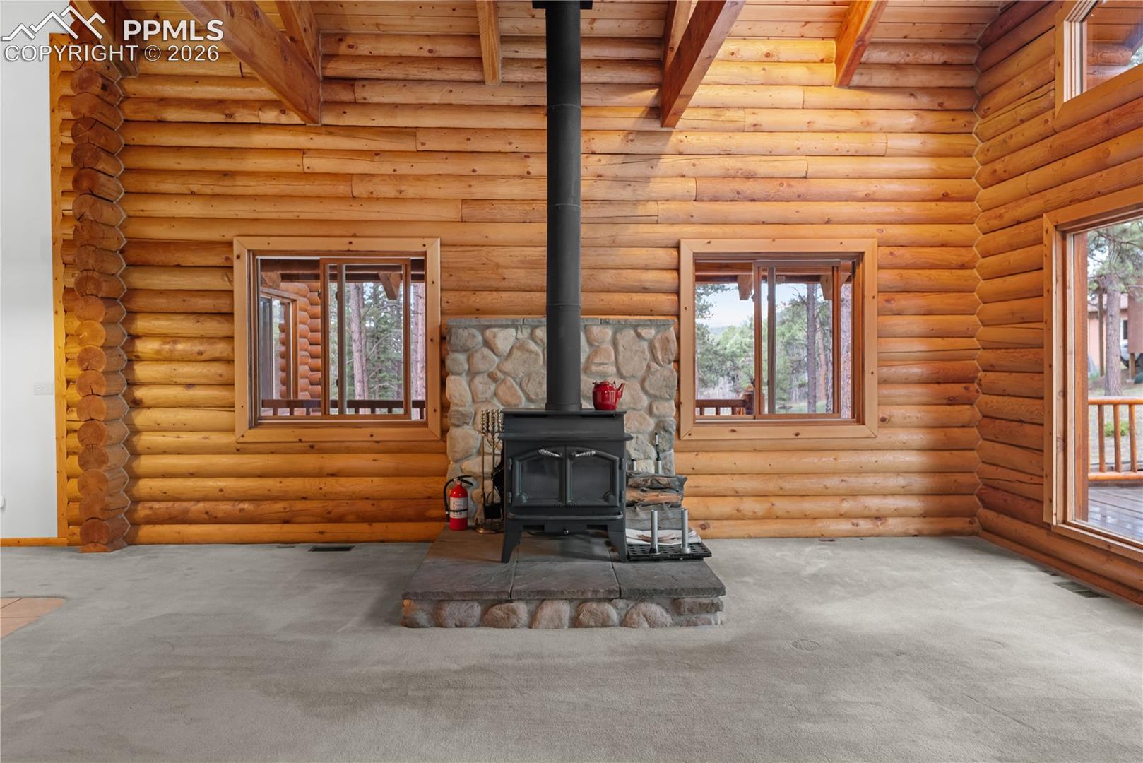 Unfurnished living room featuring a wood stove, carpet, log walls, and a wood ceiling with exposed beams