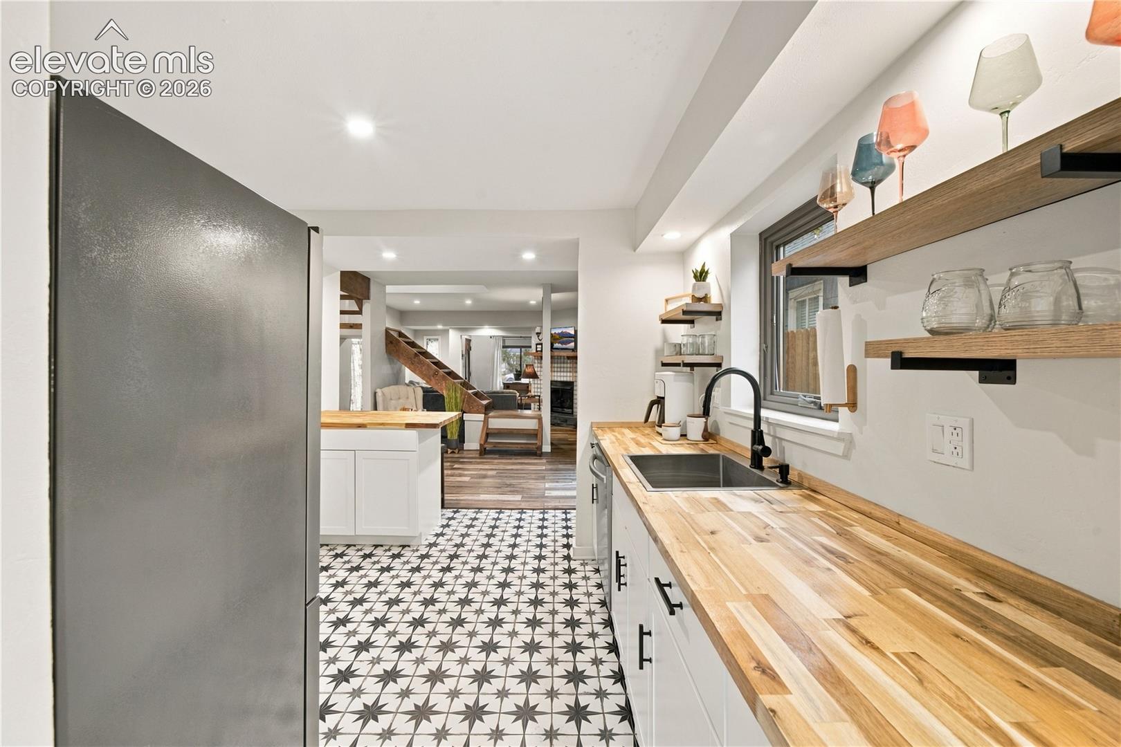 Kitchen featuring butcher block countertops, white cabinetry with matte black hardware, patterned tile flooring, an undermount sink with a matte black faucet, and natural wood-finish open shelving