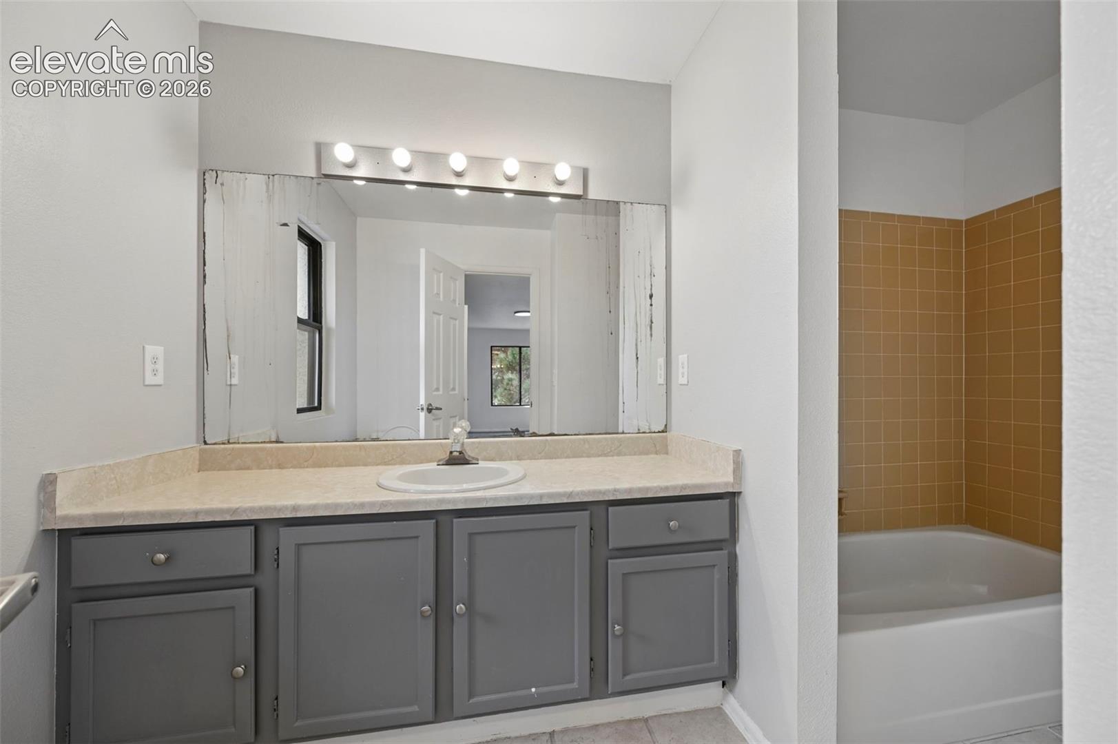 Vanity with integrated sink, light-colored countertop, and gray cabinetry with silver hardware