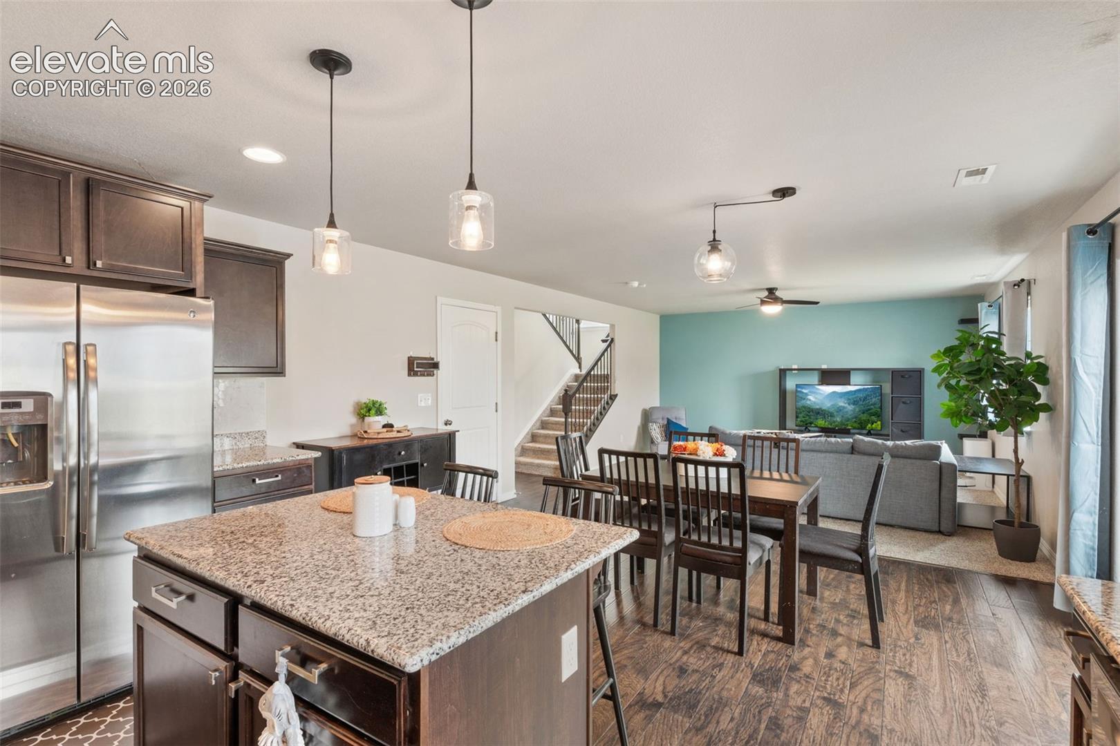 Kitchen island with a granite countertop, wood-finish flooring, recessed lighting, and modern pendant lights